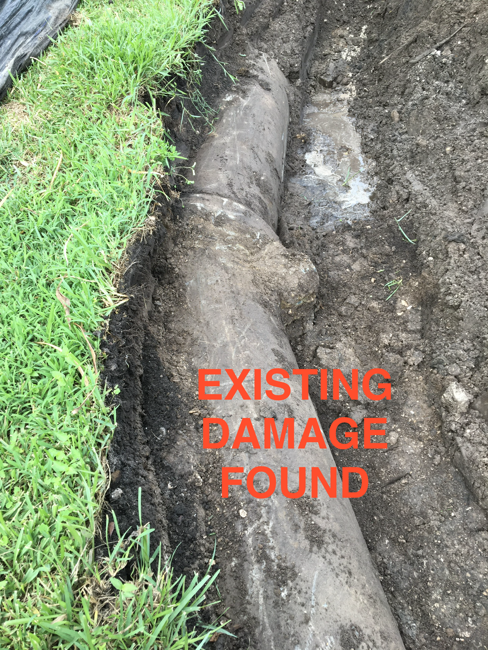 A dug trench in the ground with an underground pipe exposed, alongside green grass. The image has a warning overlay in bold red text that says 'EXISTING DAMAGE FOUND'.