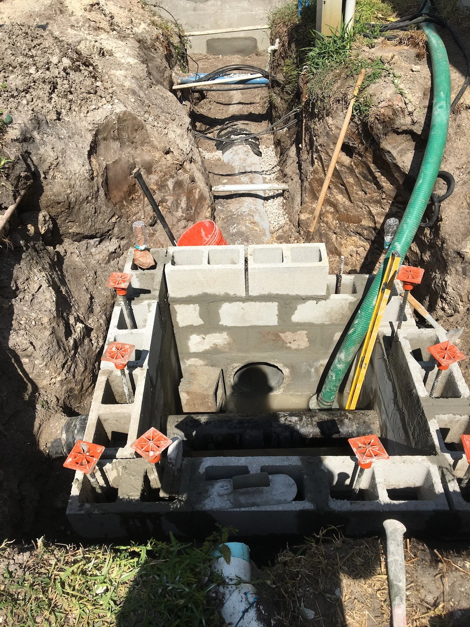 Construction site with a partially built concrete structure, pipes, and supporting tools in an excavation trench.  Utility conflict structure.