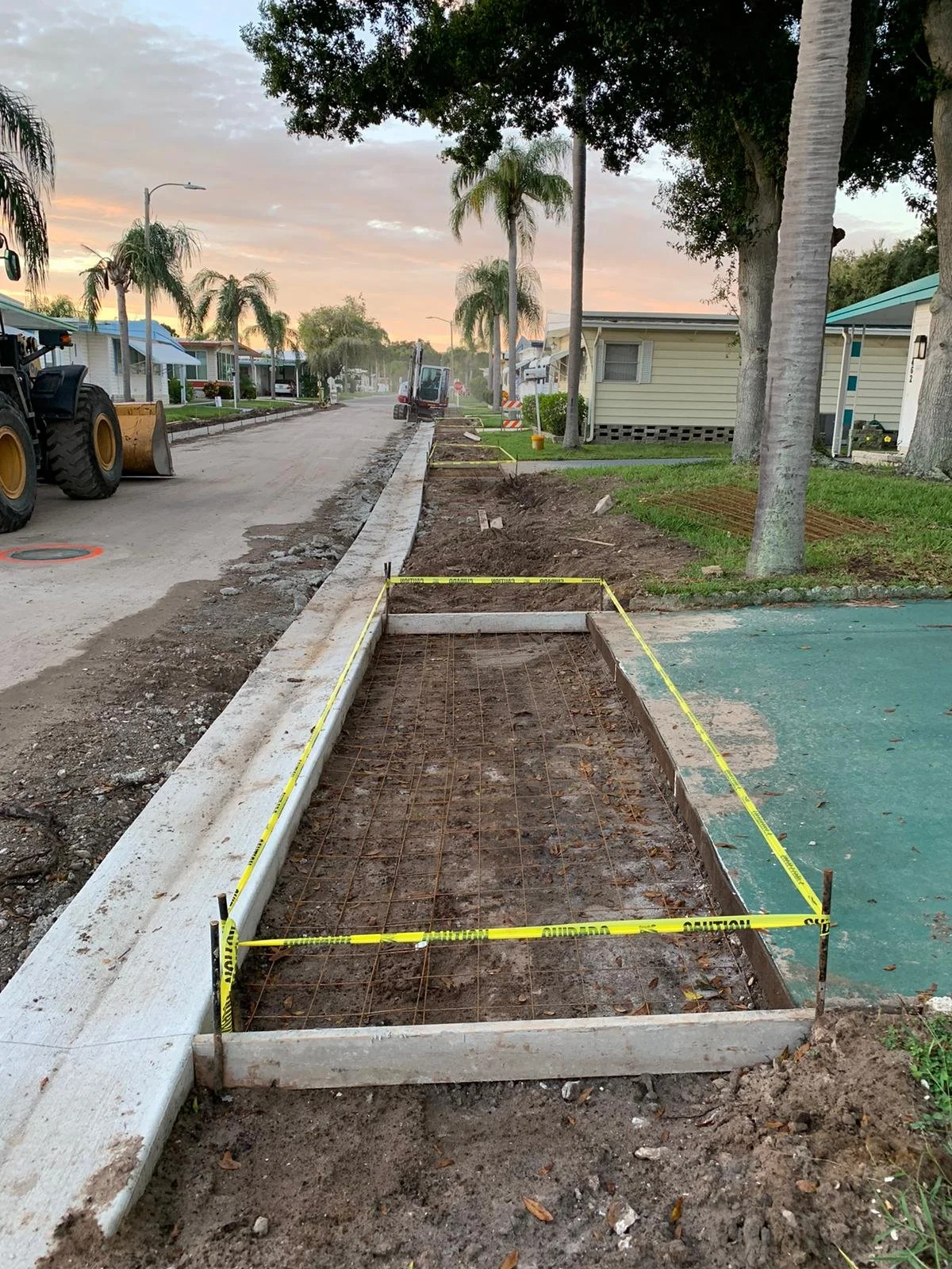 Construction site on a residential street with tools, equipment, and survey marked area for sidewalk or road work at sunset. Concrete driveway installation.