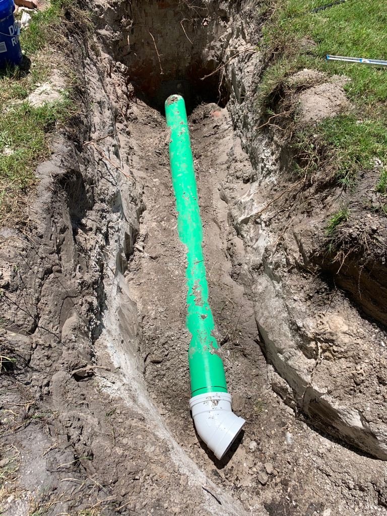 Green and white PVC pipe installed in a trench in the ground during a construction project.