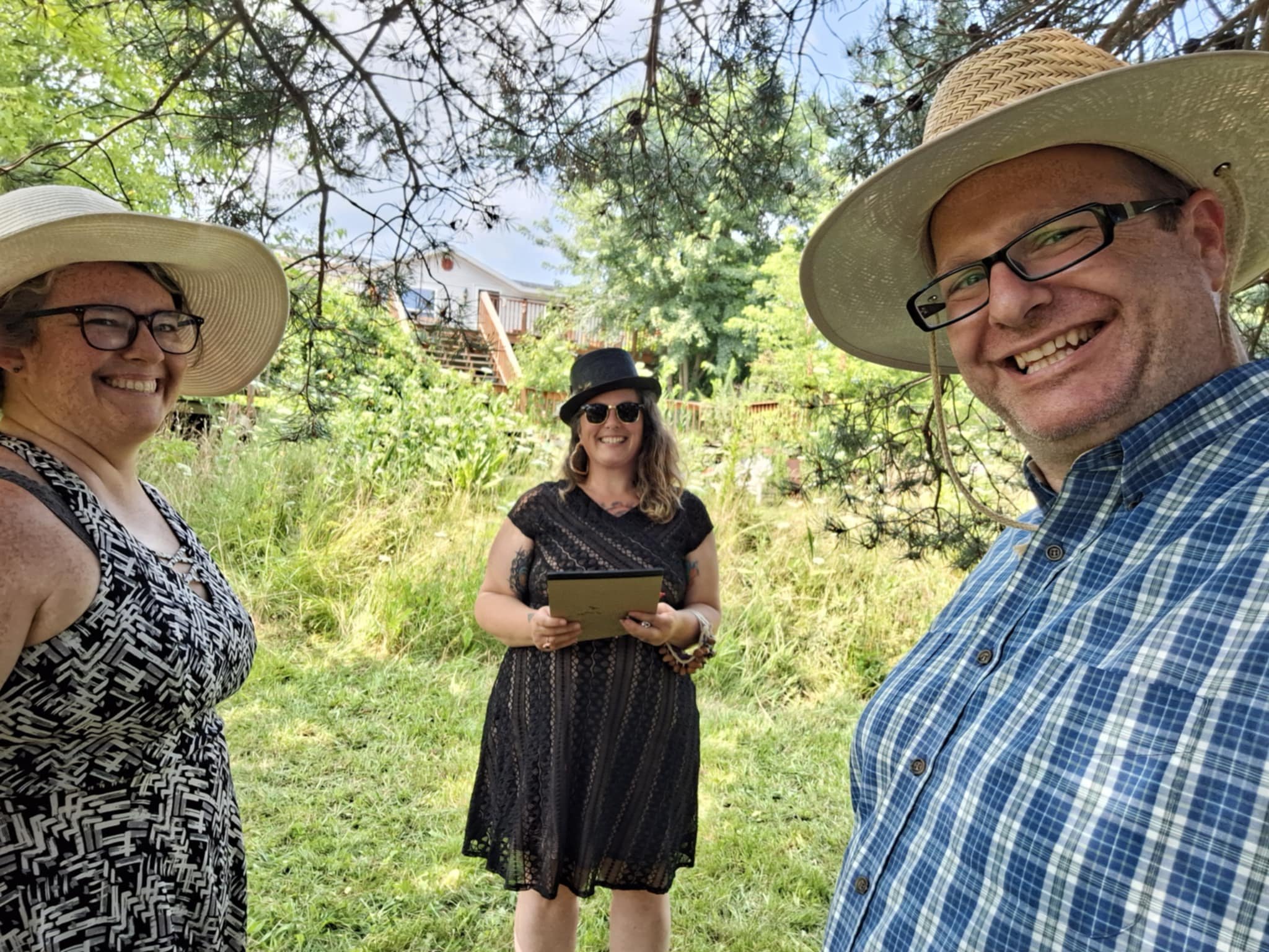 Two women and one man standing outdoors under tree branches, smiling for a selfie. 