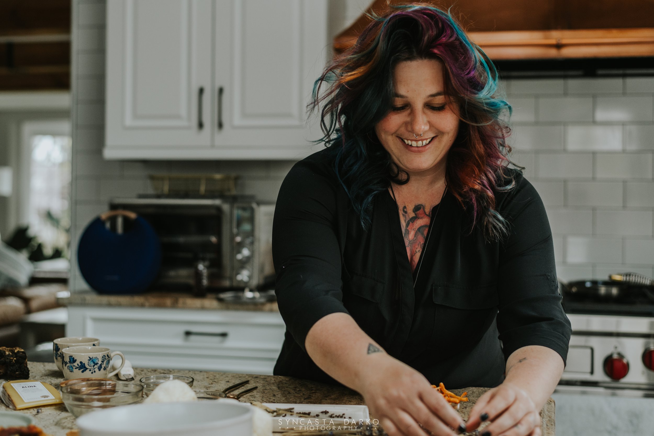 A woman with colorful hair and tattoos is preparing food in a modern kitchen.