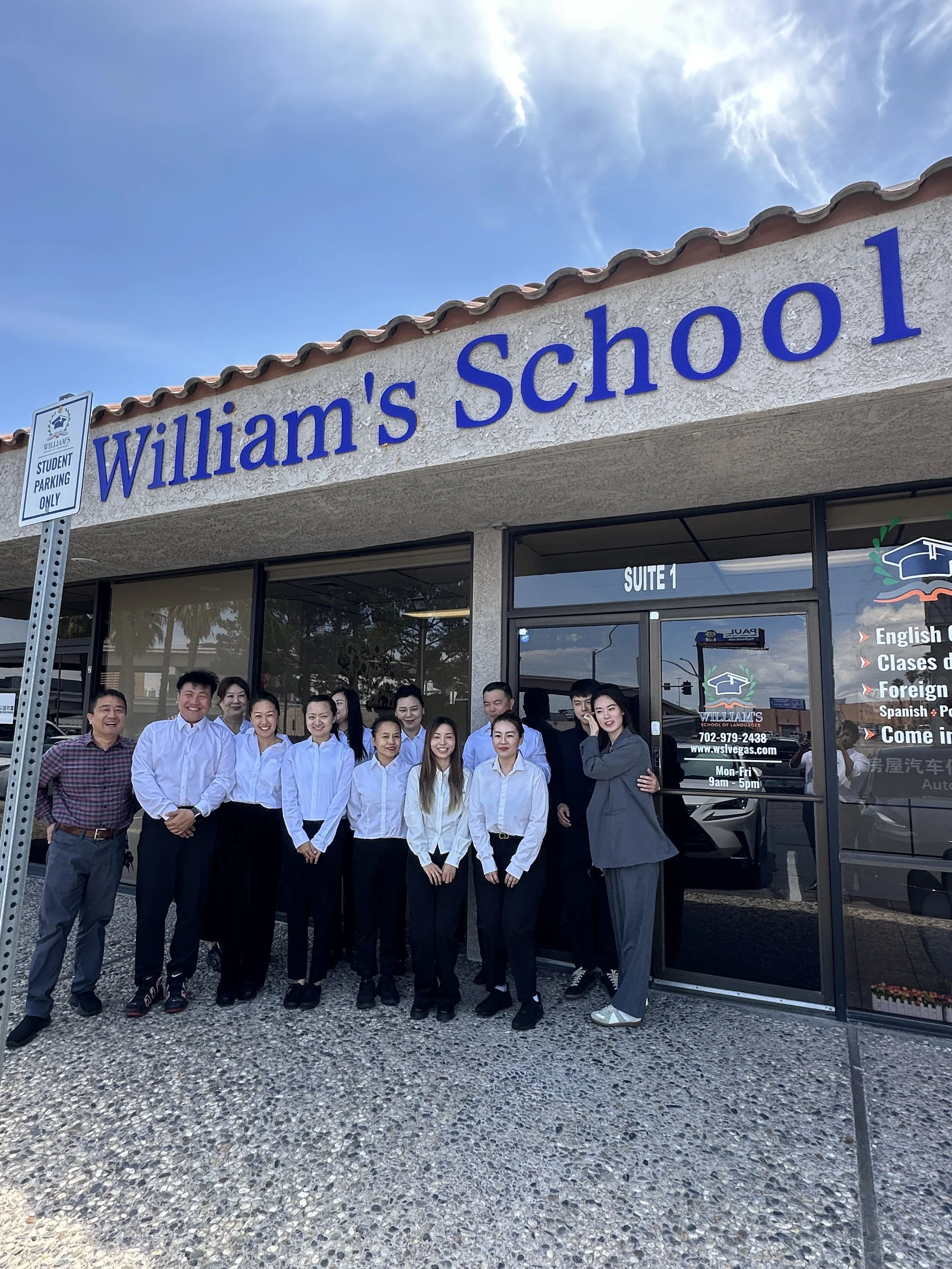 Group of people standing outside of Williams School of Languages in front of the building entrance, smiling and posing for a photo on a sunny day.