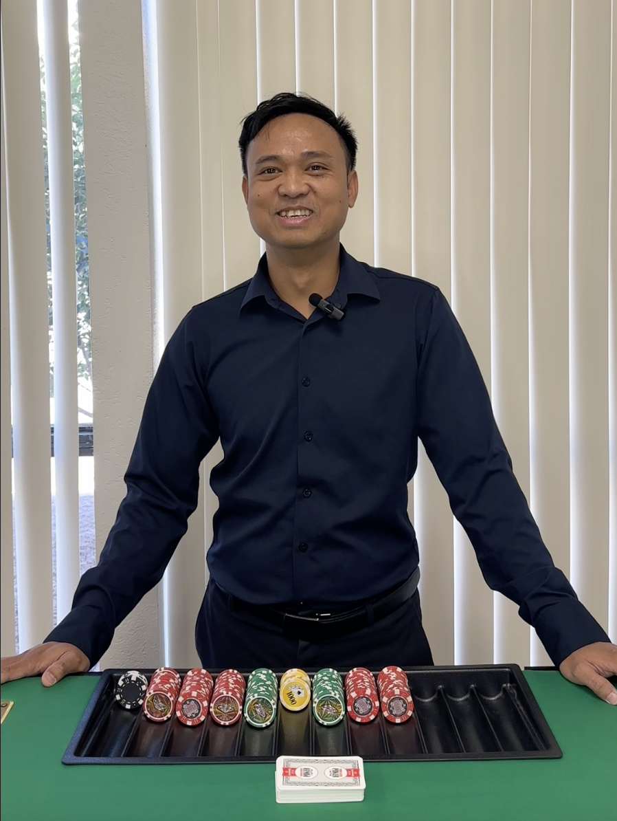 Man smiling standing behind a poker table with stacked poker chips.