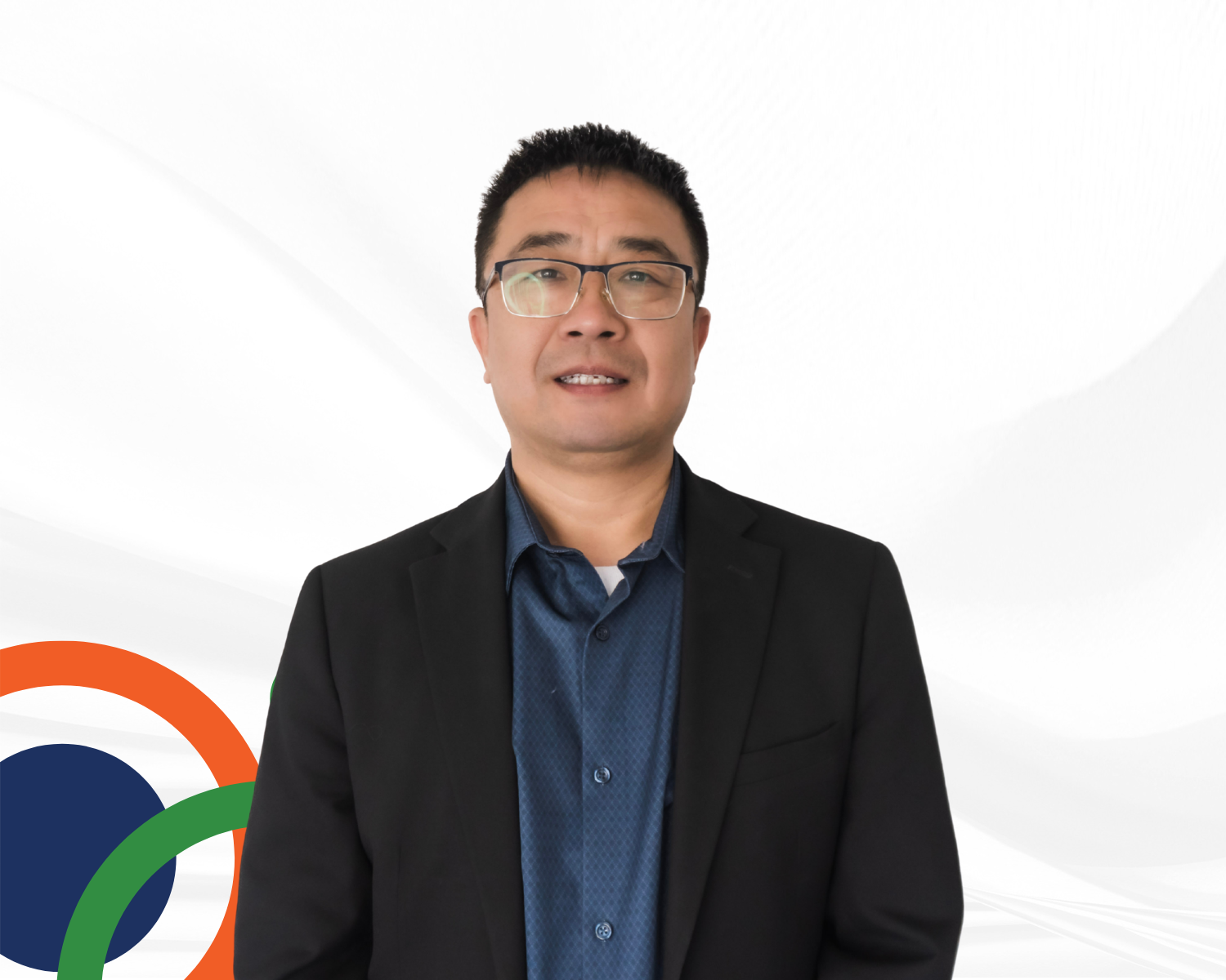 A man in glasses wearing a black suit over a blue shirt, standing against a white background with a partial Google logo in the bottom left corner.