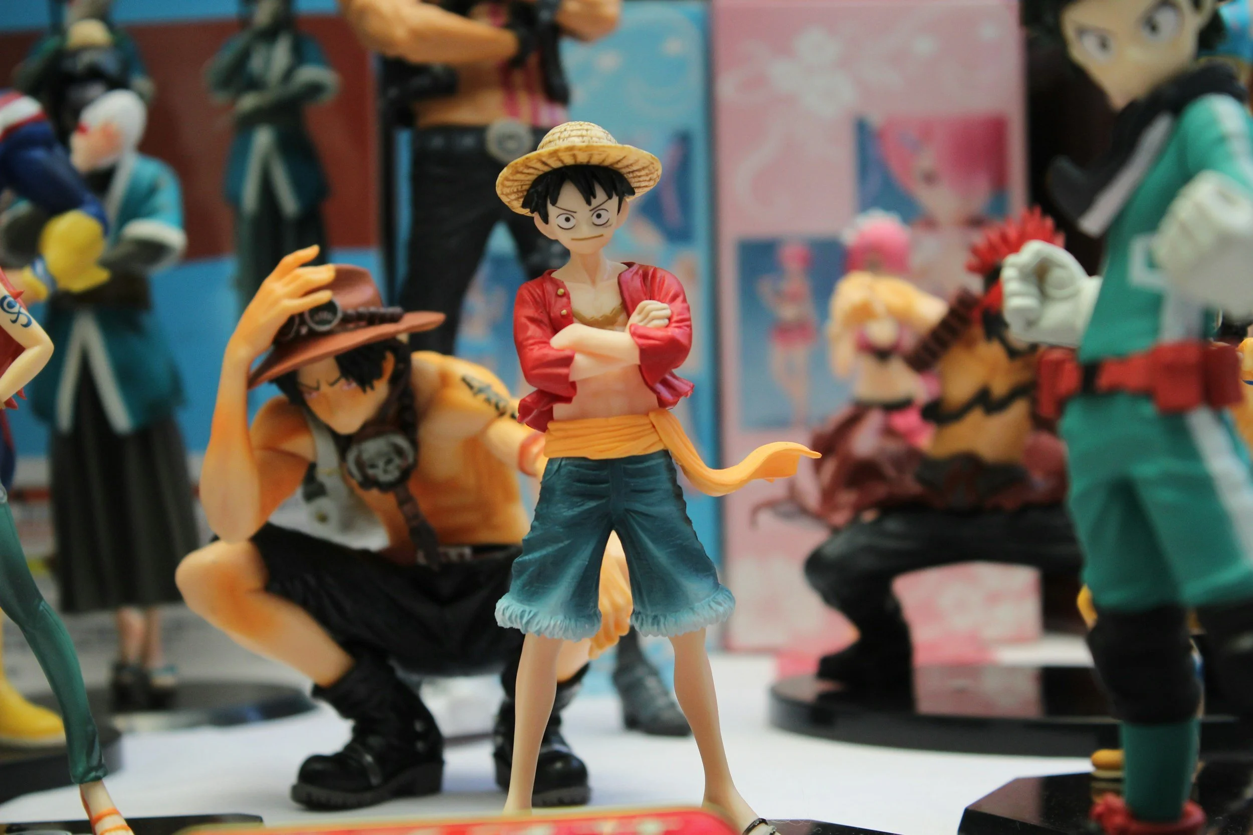 Plastic figurines of characters from the anime 'One Piece' on display, including Monkey D. Luffy in the center wearing a straw hat, red shirt, and blue pants, with other characters around him in various poses and costumes.