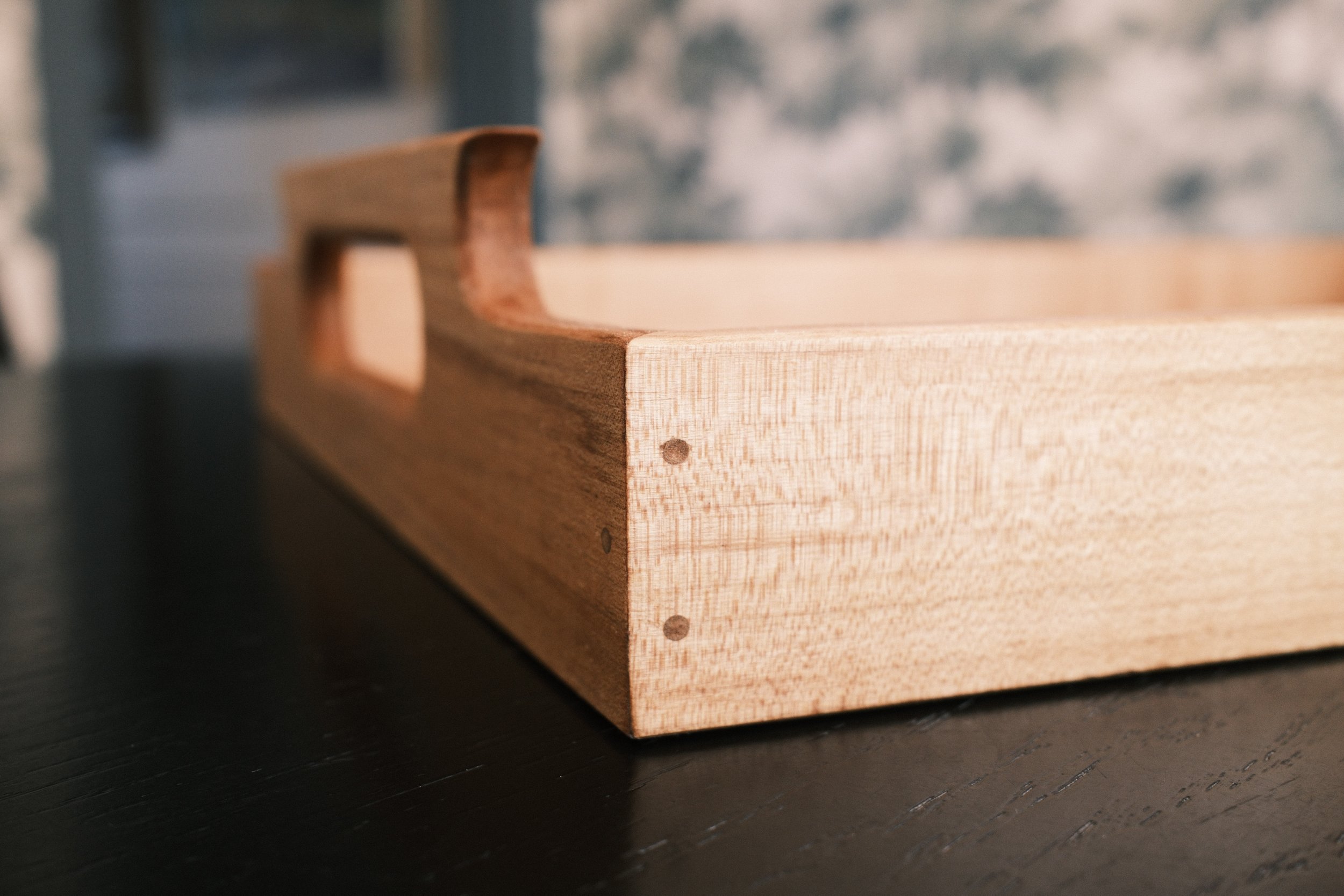 Close-up of a handmade wooden tray with expert joinery, visible knots and grains, placed on a dark surface.