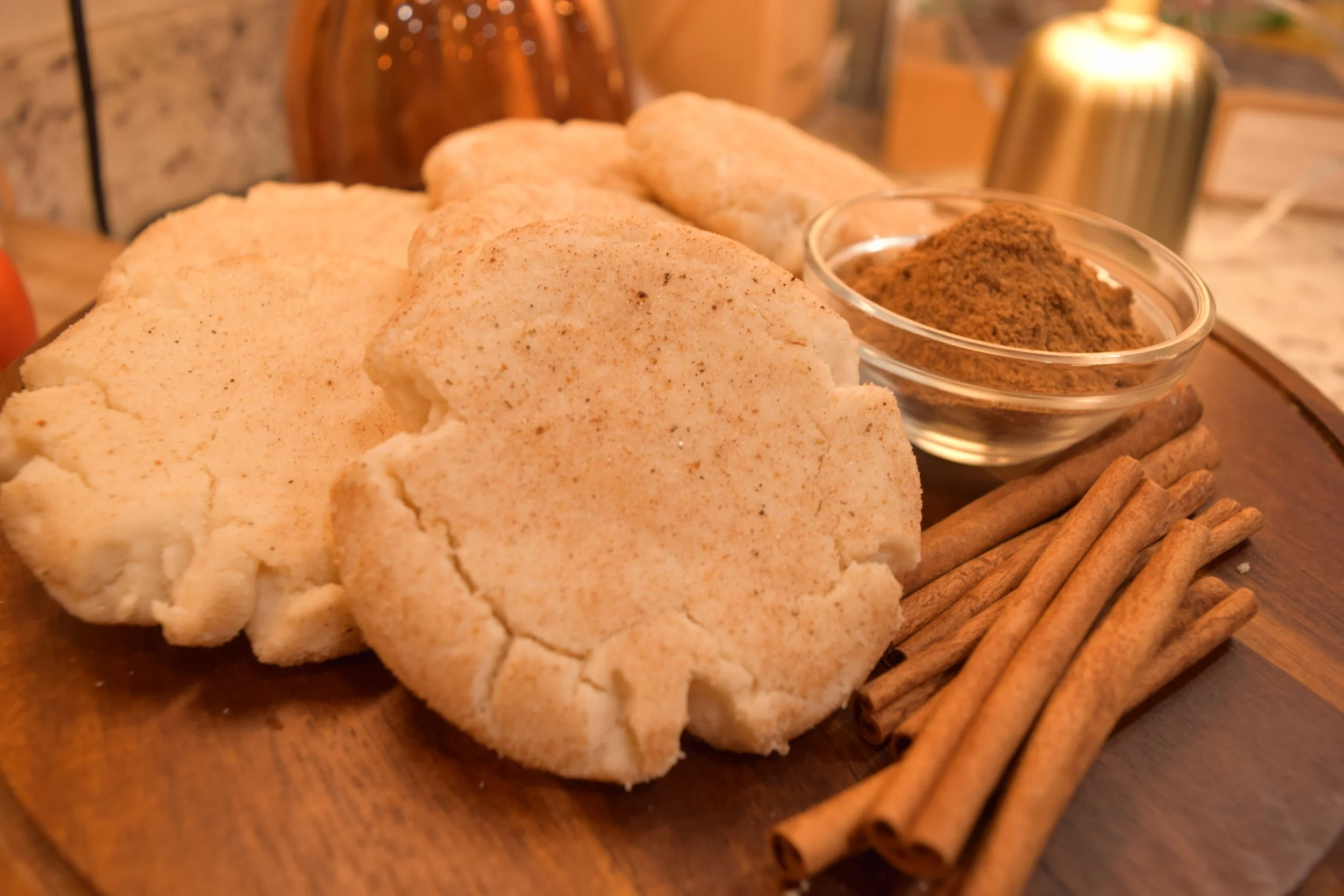 Baharat snickerdoodles on a wooden board with cinnamon sticks and a bowl of baharat spice
