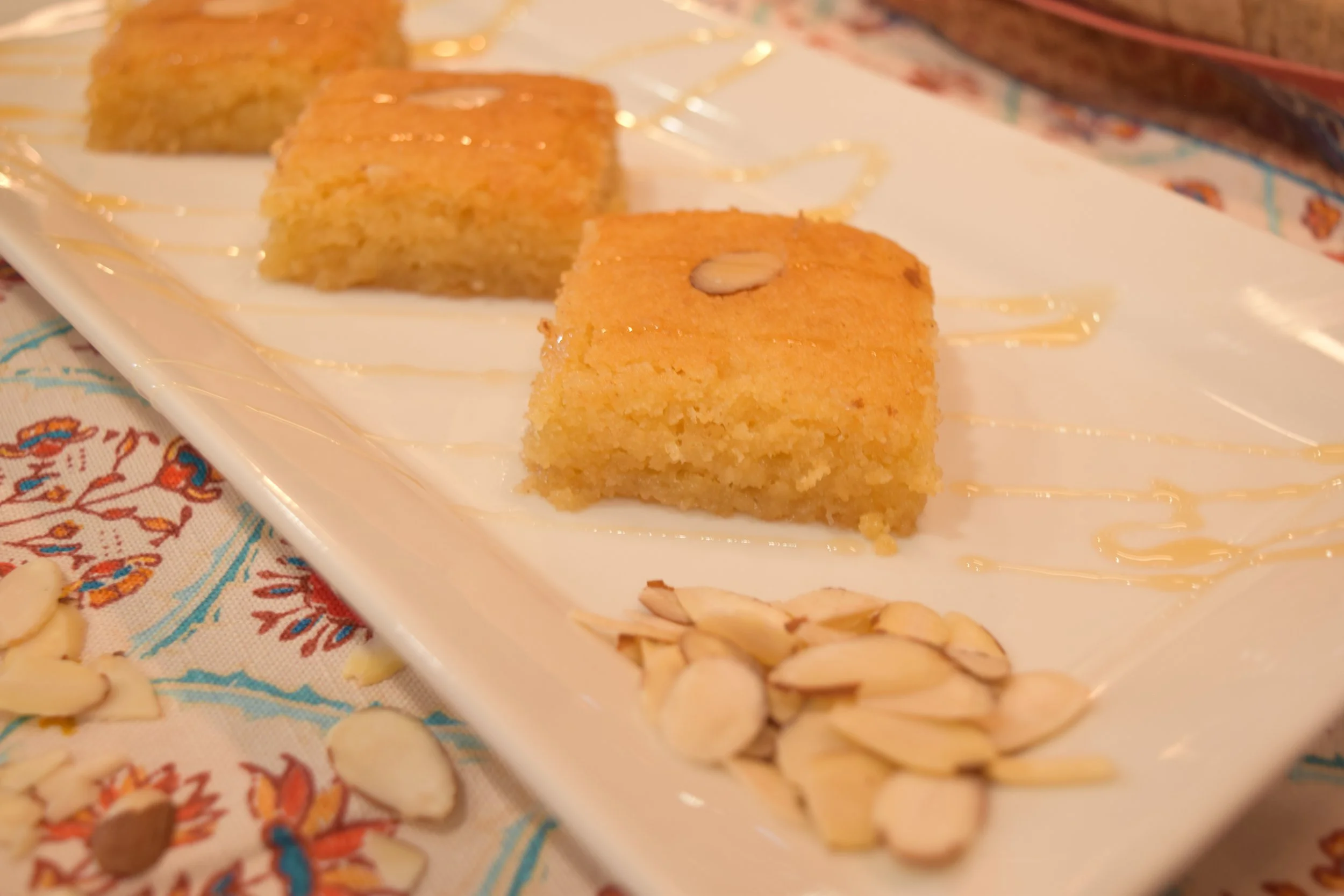 Namoura honey semolina cake squares topped with almonds on a white plate