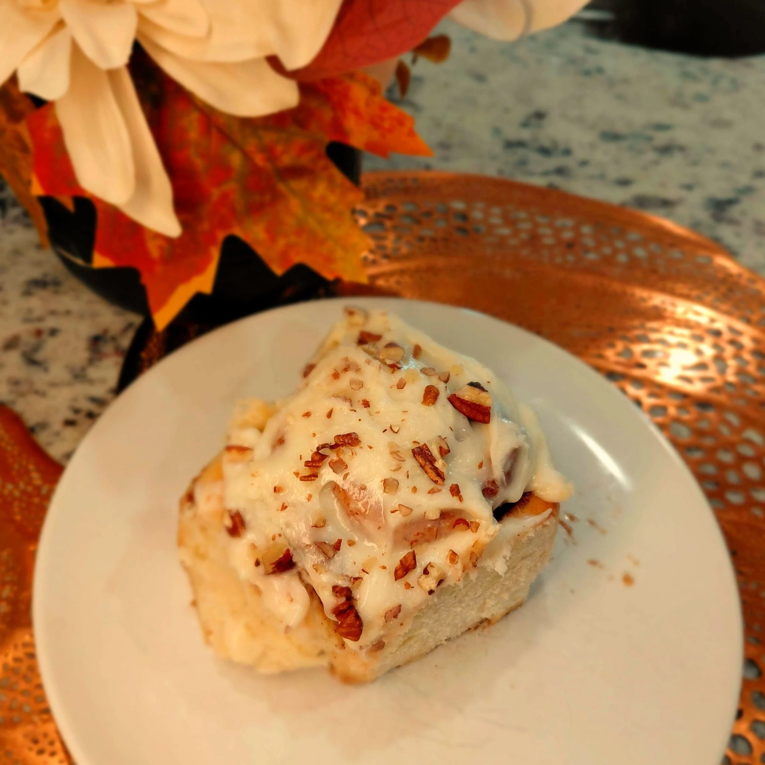 Cinnamon roll with cream cheese frosting and chopped pecans on a copper tray