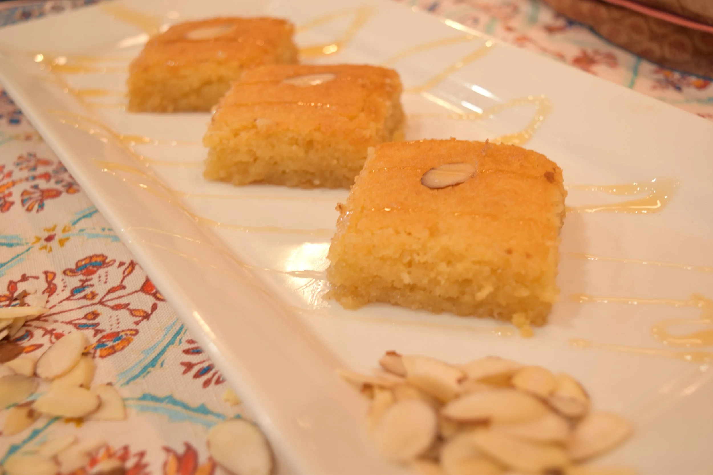 Namoura honey semolina cake squares topped with almonds on a white plate