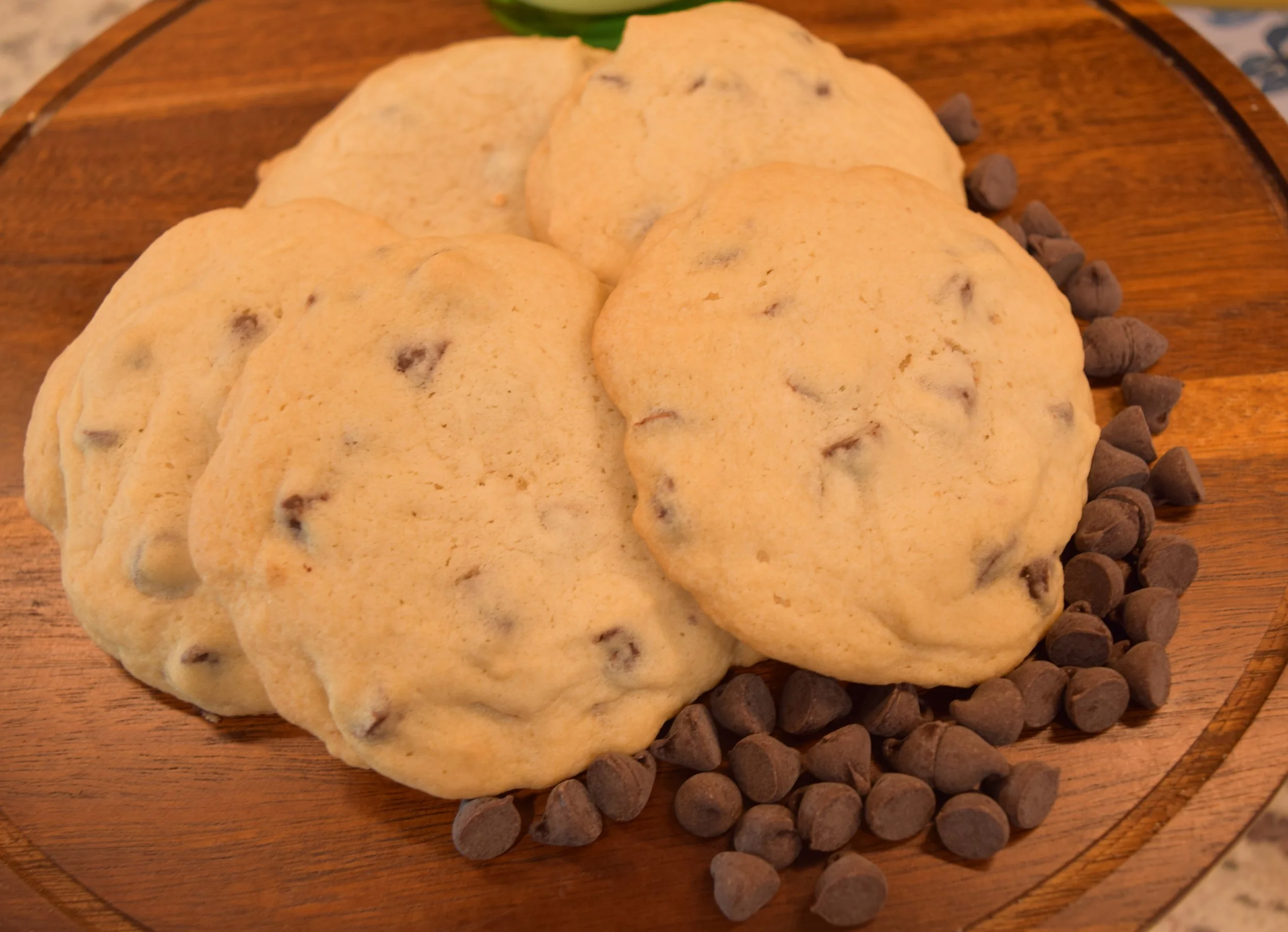 Chocolate chip cookies on a round wooden board with chocolate chips scattered beside them