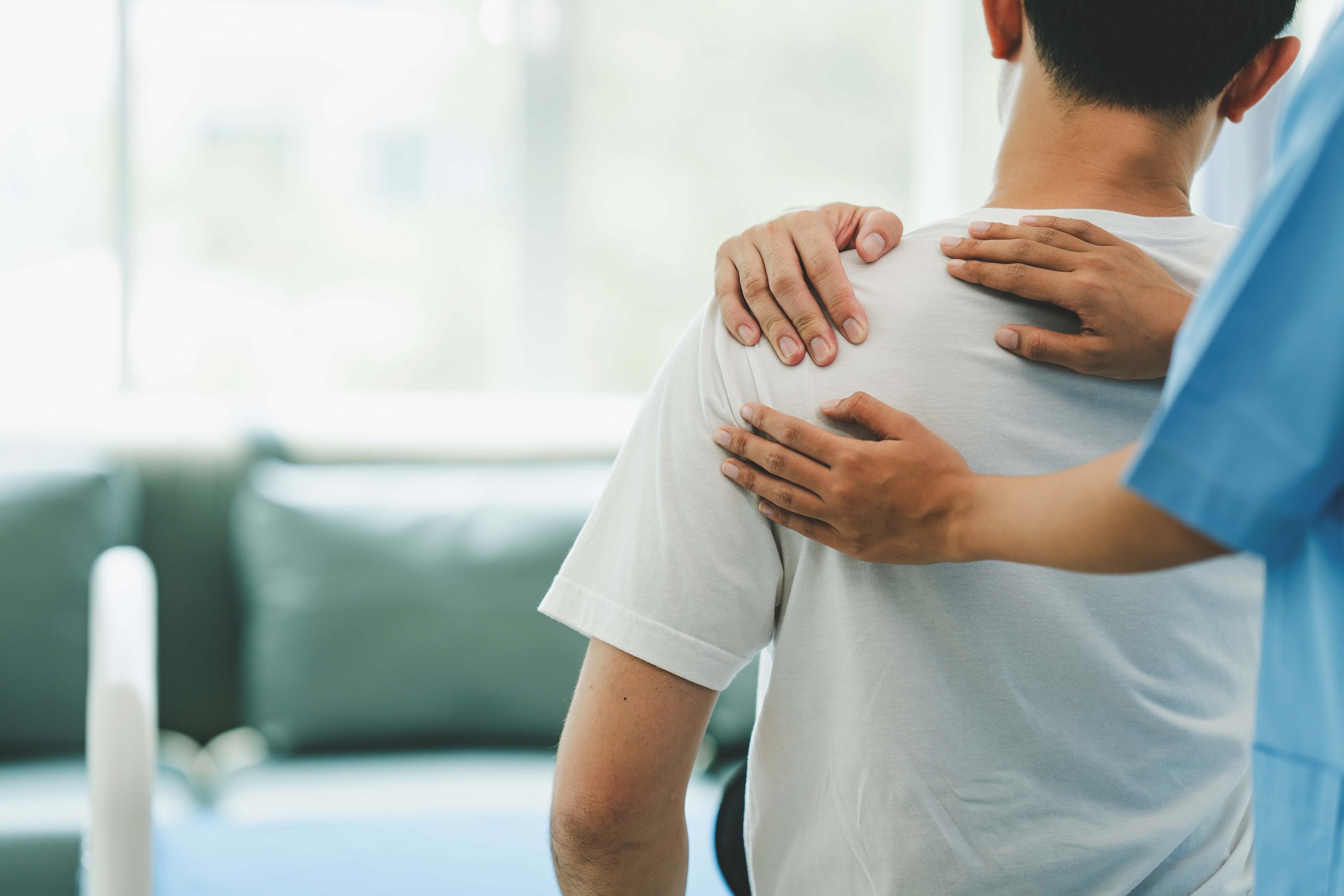 A person in a blue medical uniform comforting a patient who is experiencing shoulder pain or discomfort in a healthcare setting.
