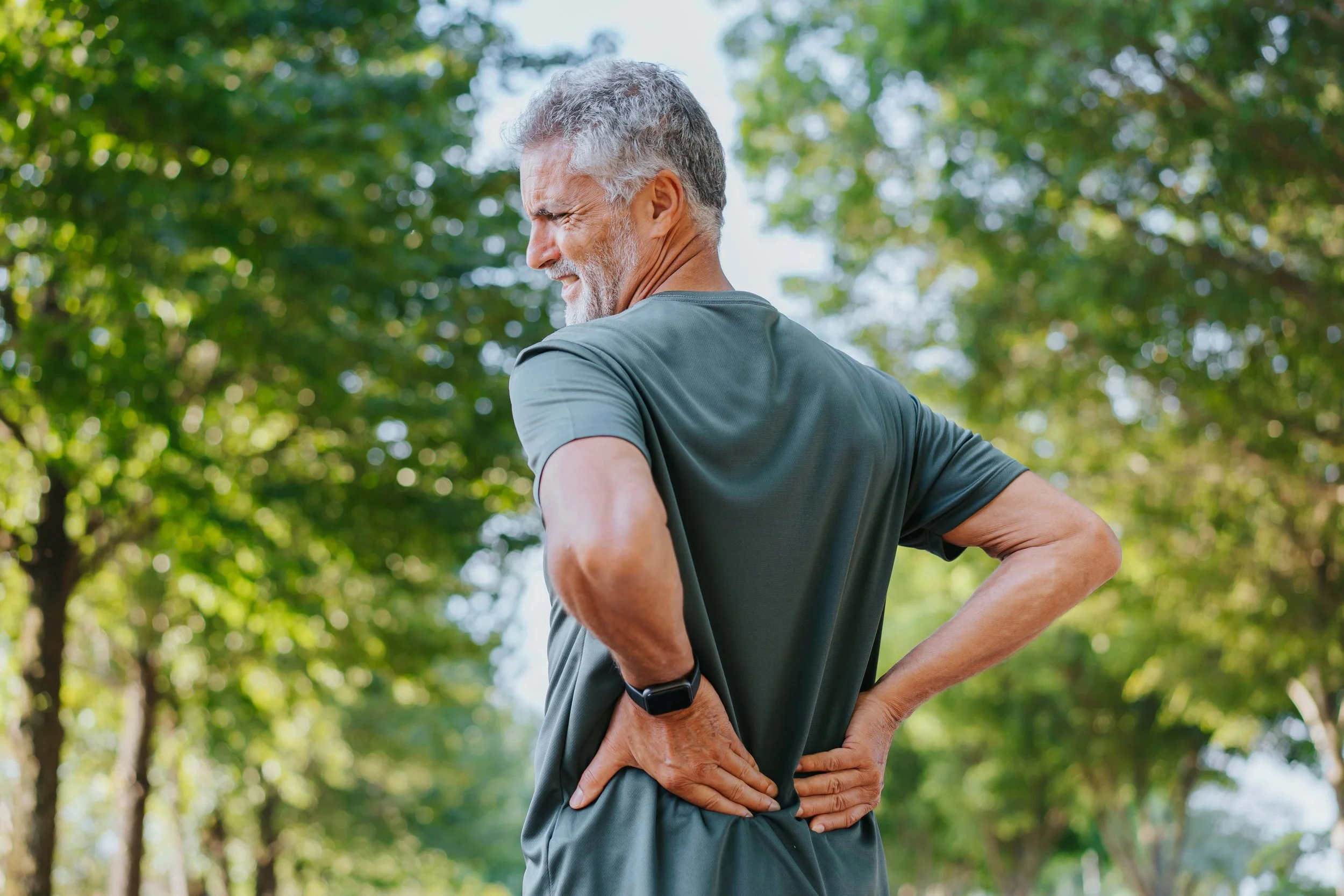 Older man in athletic clothing stretching outdoors in a park on a sunny day