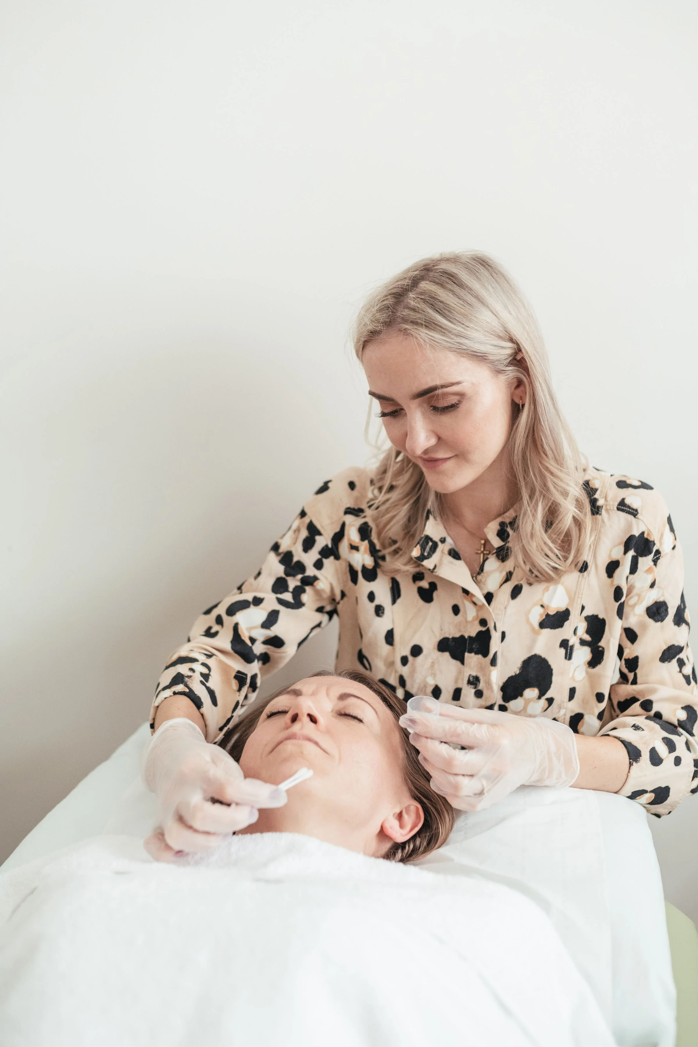 A woman receiving a facial treatment from a skincare professional in a clinical setting.