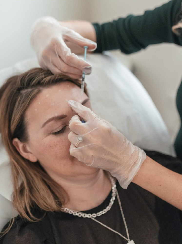 A woman receiving a cosmetic injection in her forehead from a medical professional wearing gloves.