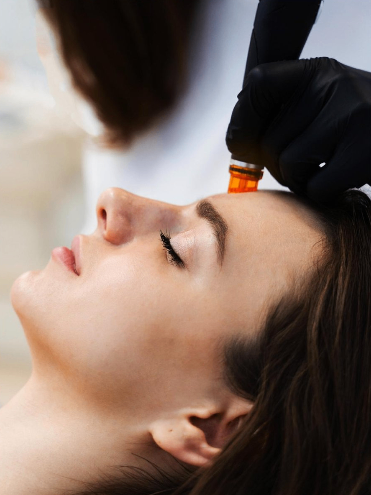 Close-up of a woman receiving a cosmetic treatment using a microcurrent device, performed by a professional wearing black gloves.
