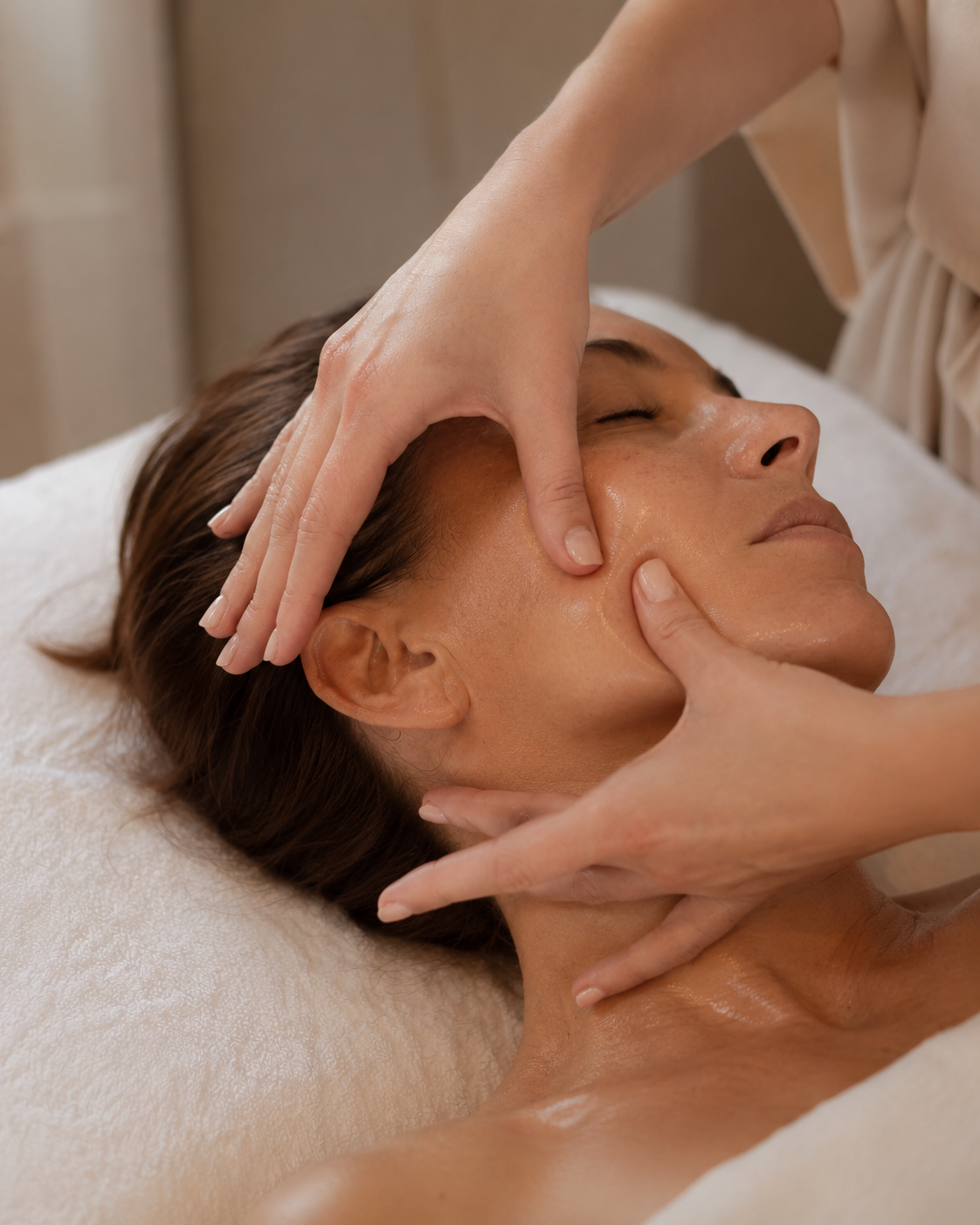 Person receiving a facial massage in a spa setting, lying on a massage table with eyes closed.