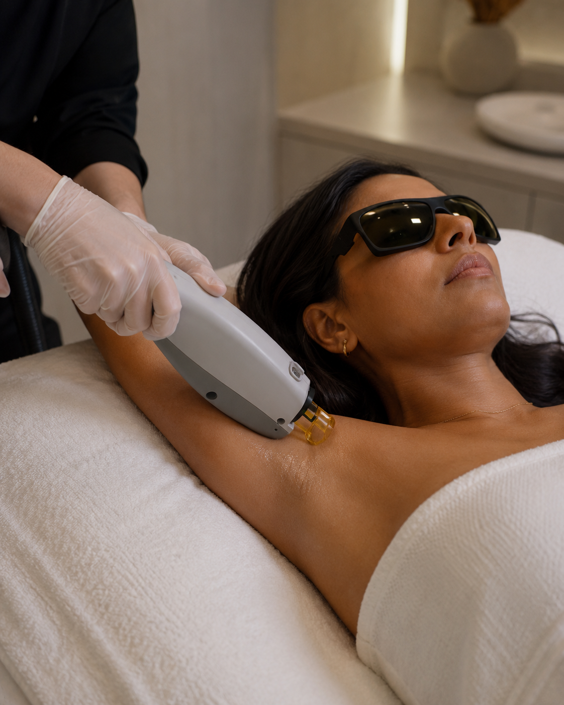 Woman receiving laser hair removal therapy on her underarm, wearing protective glasses, in a spa or clinic.