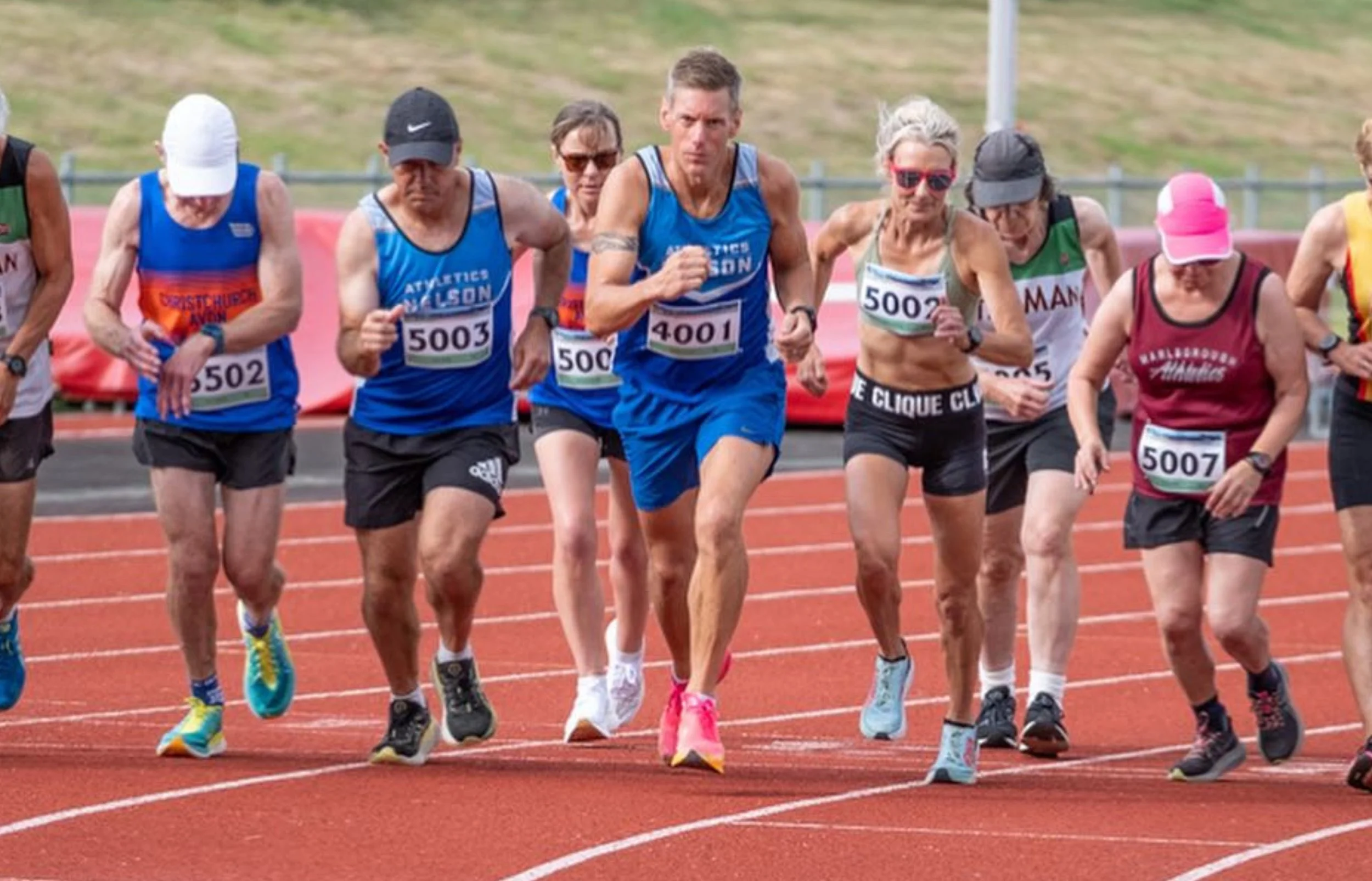 A group of runners competing in a track race, wearing athletic gear and race bibs.