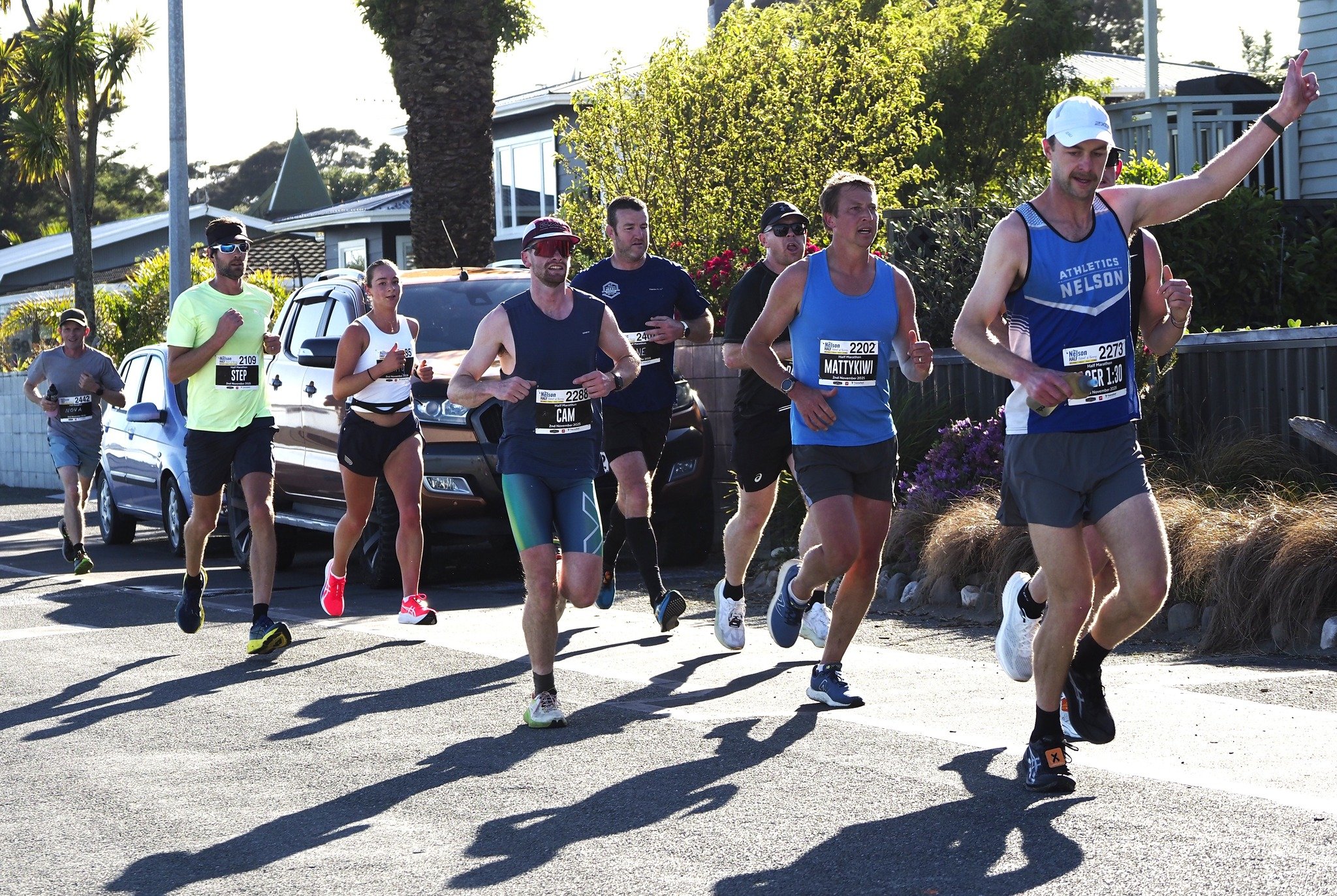 Group of runners participating in a race, running along a street in a residential neighborhood during daytime.