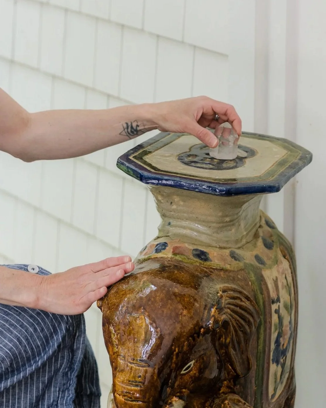 Person placing a piece of ice on top of a ceramic or stone fountain or sculpture of an elephant.