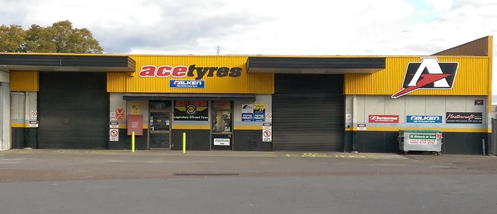 Exterior view of a store named Ace Tyres selling tires, with signs for Falken, Bridgestone, and other tire brands, and a large yellow and black facade.