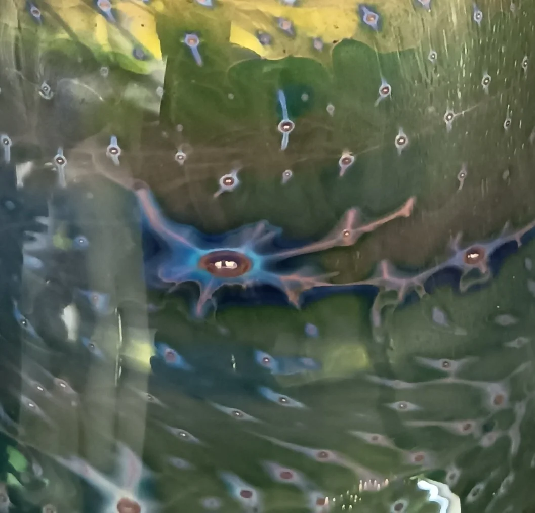 A close-up view of a large blue and purple newt with a slightly open mouth. The newt's body is reflected in water, which is covered with numerous small bubbles or water droplets.