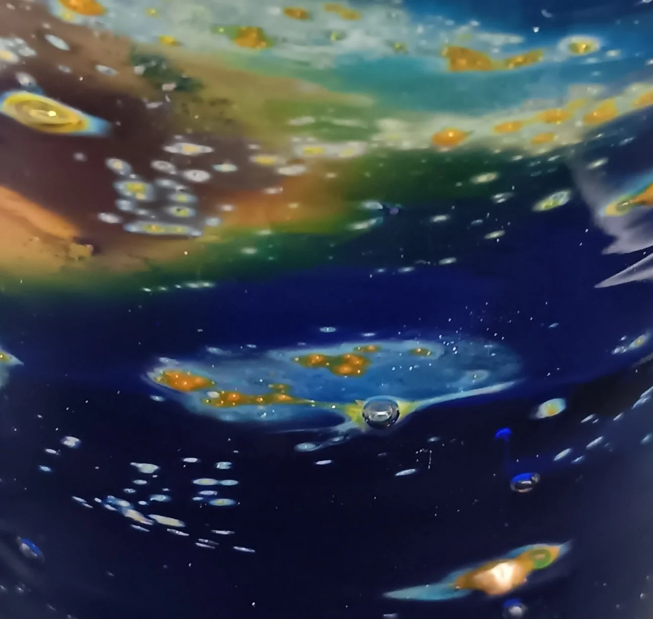 Close-up of the water surface with bubbles and colorful reflections beneath.