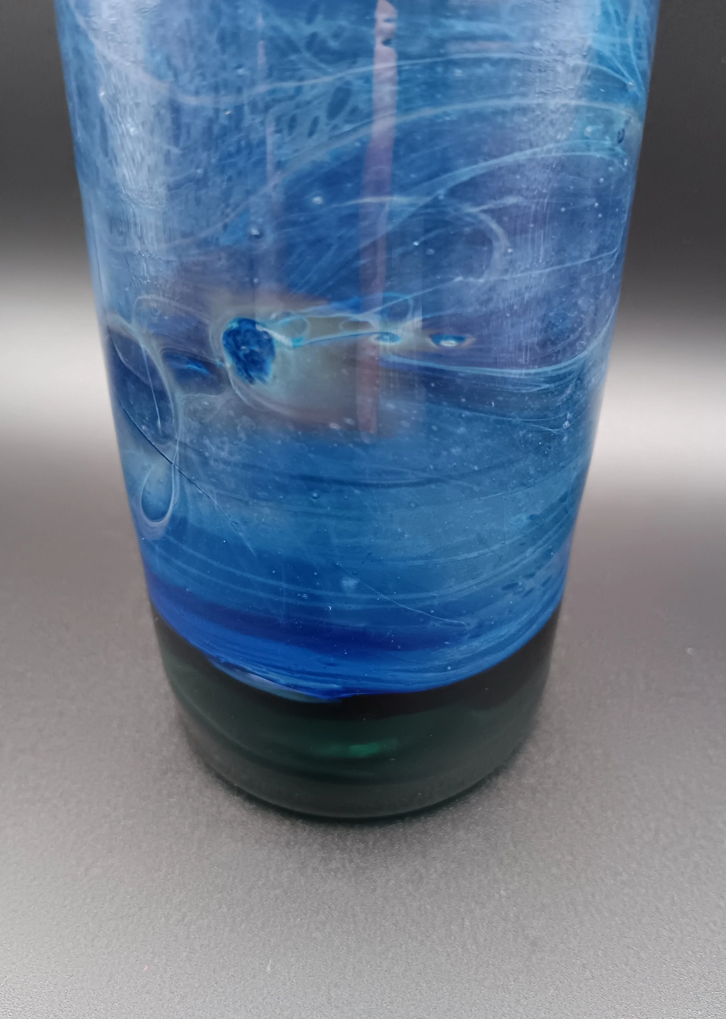 Close-up of a blue swirling glass with a dark base on a gray surface.
