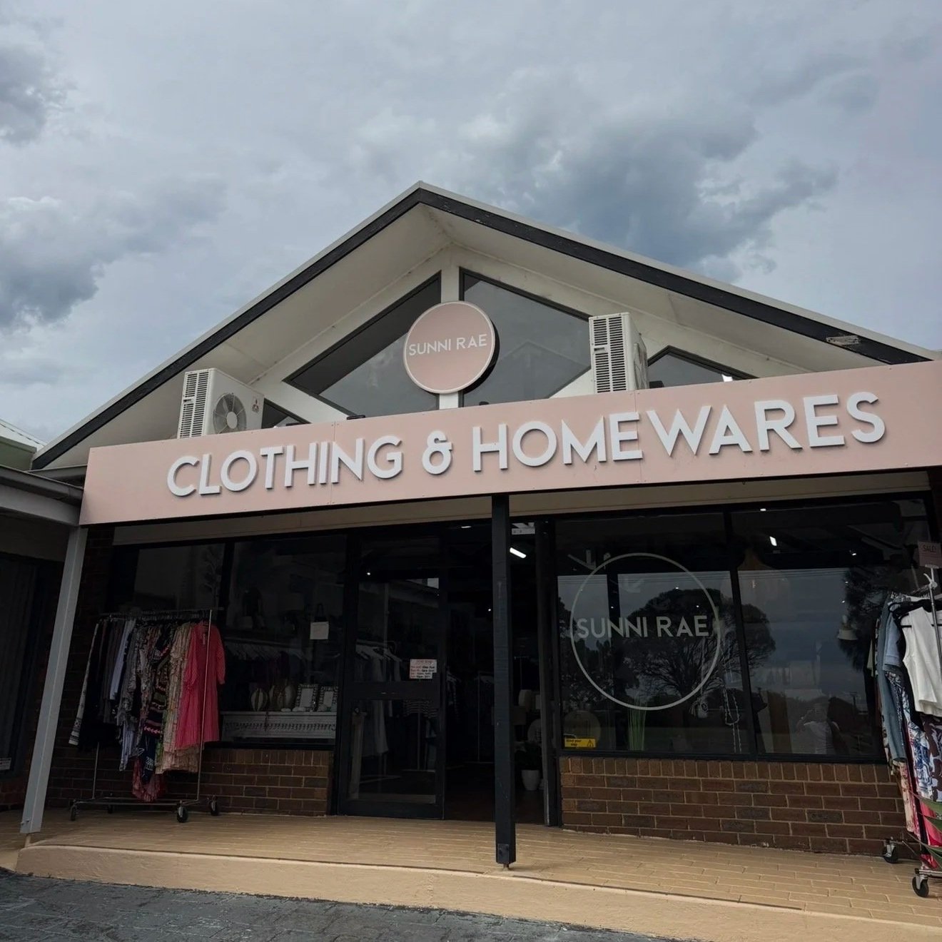 Clothing and homewares store named Sunni Rae with a pink sign and clothing racks outside