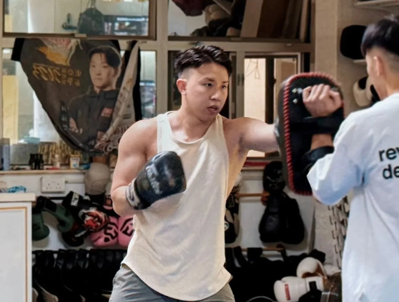 A young man training in boxing with a coach in a gym, practicing punches with boxing gloves on.