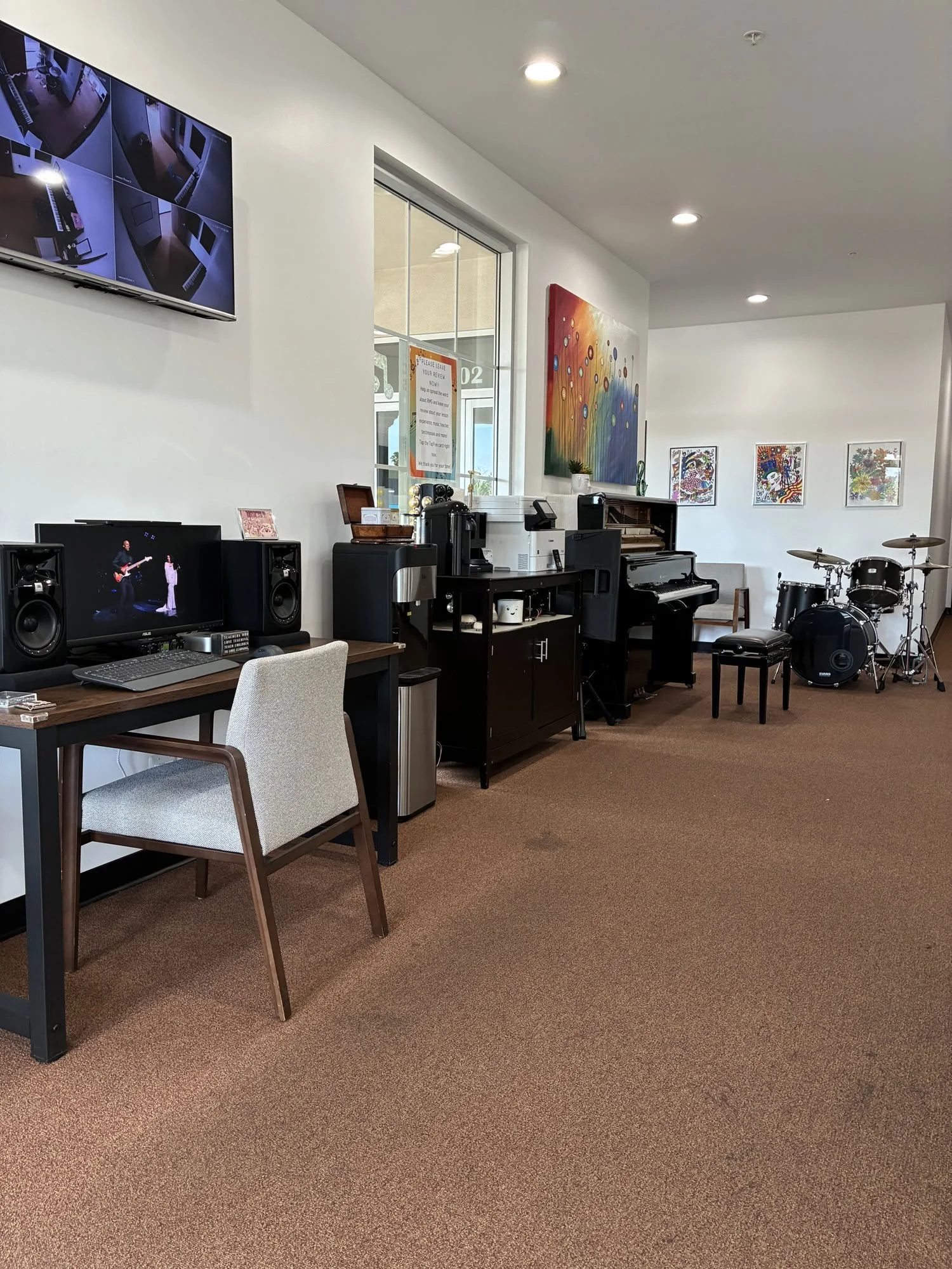 A room with a computer desk, music equipment, and colorful artwork on the walls.
