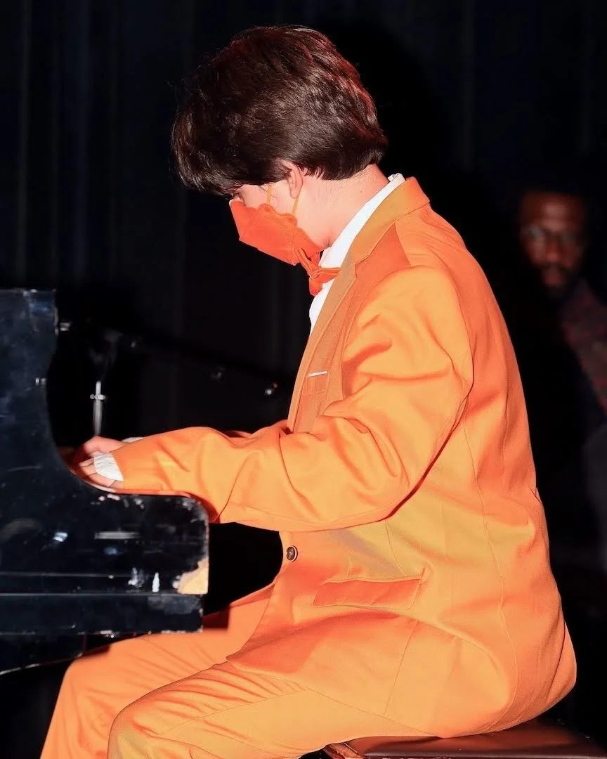 A teenage boy in an orange suit, performing at a piano recital