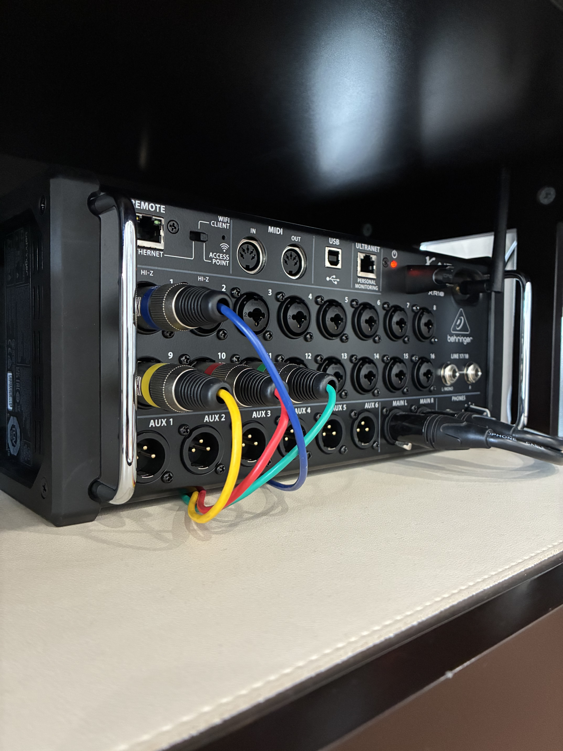 Close-up of a DJ mixer with various cables connected to input channels, placed on a beige surface with a black background.