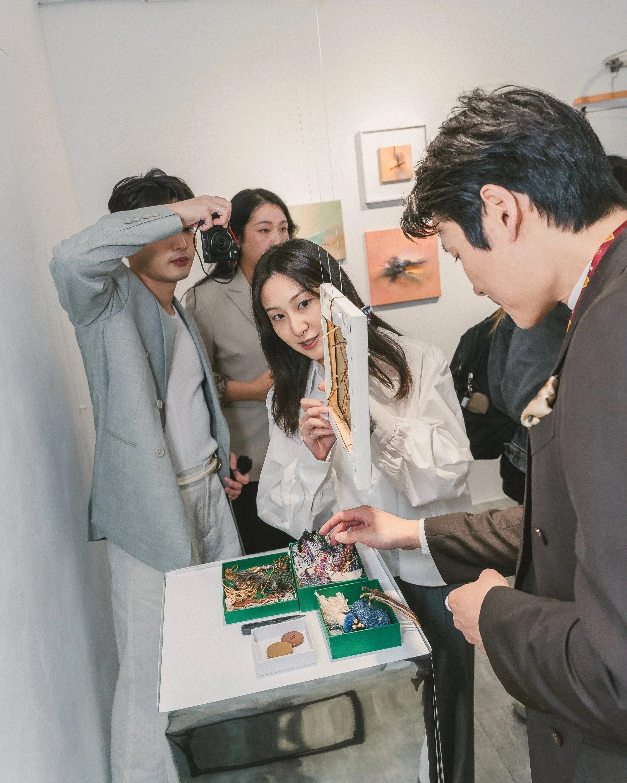 People viewing and discussing jewelry and accessories displayed on a table at an exhibition or art show.