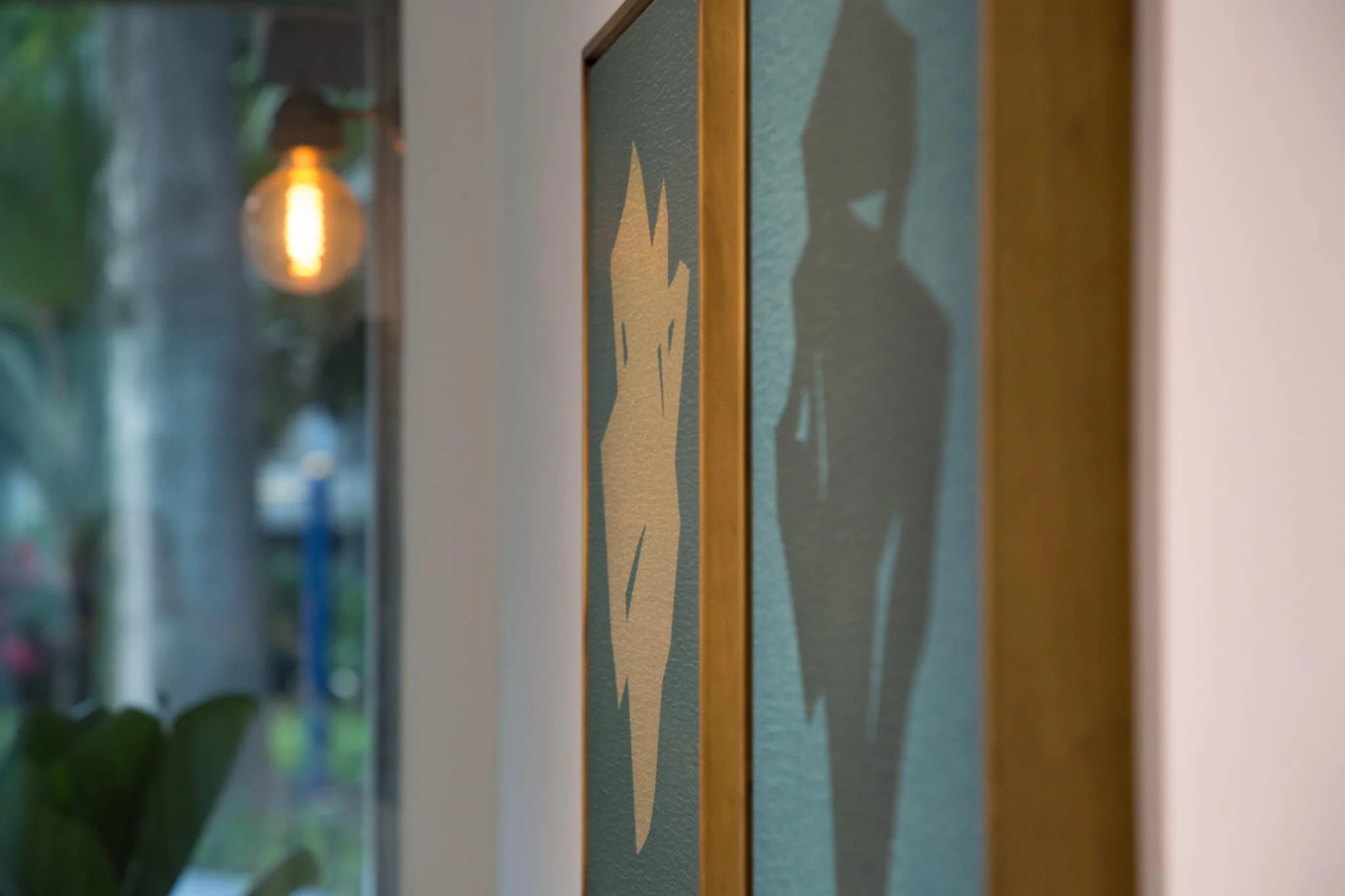 Close-up of a framed artwork on a wall with a textured background, partially reflecting a warm light fixture nearby.