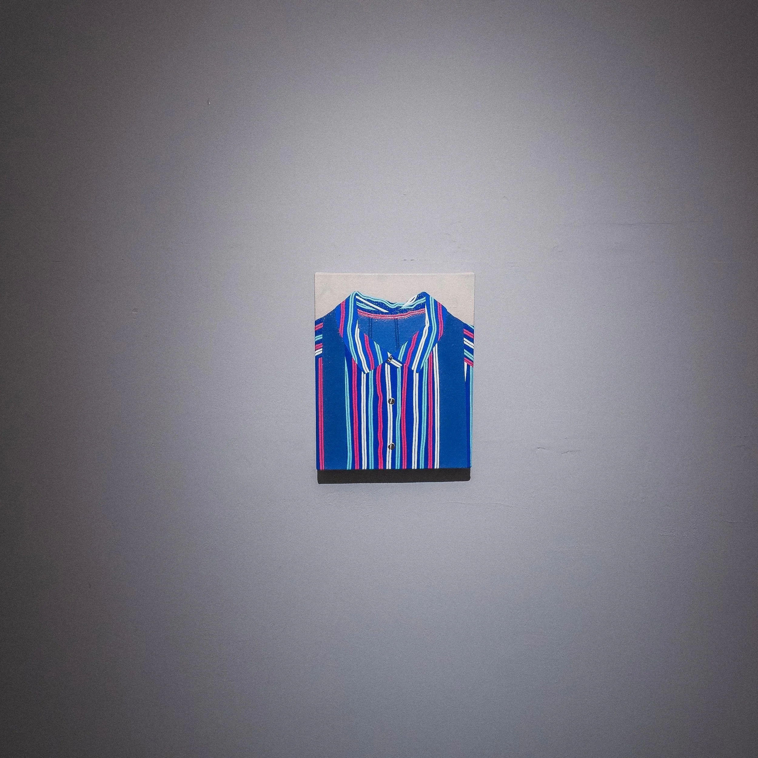 A colorful, striped blouse with buttons hanging on a gray wall.