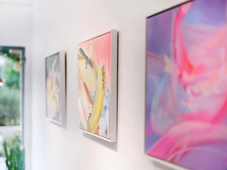 Three colorful abstract paintings on a white gallery wall.
