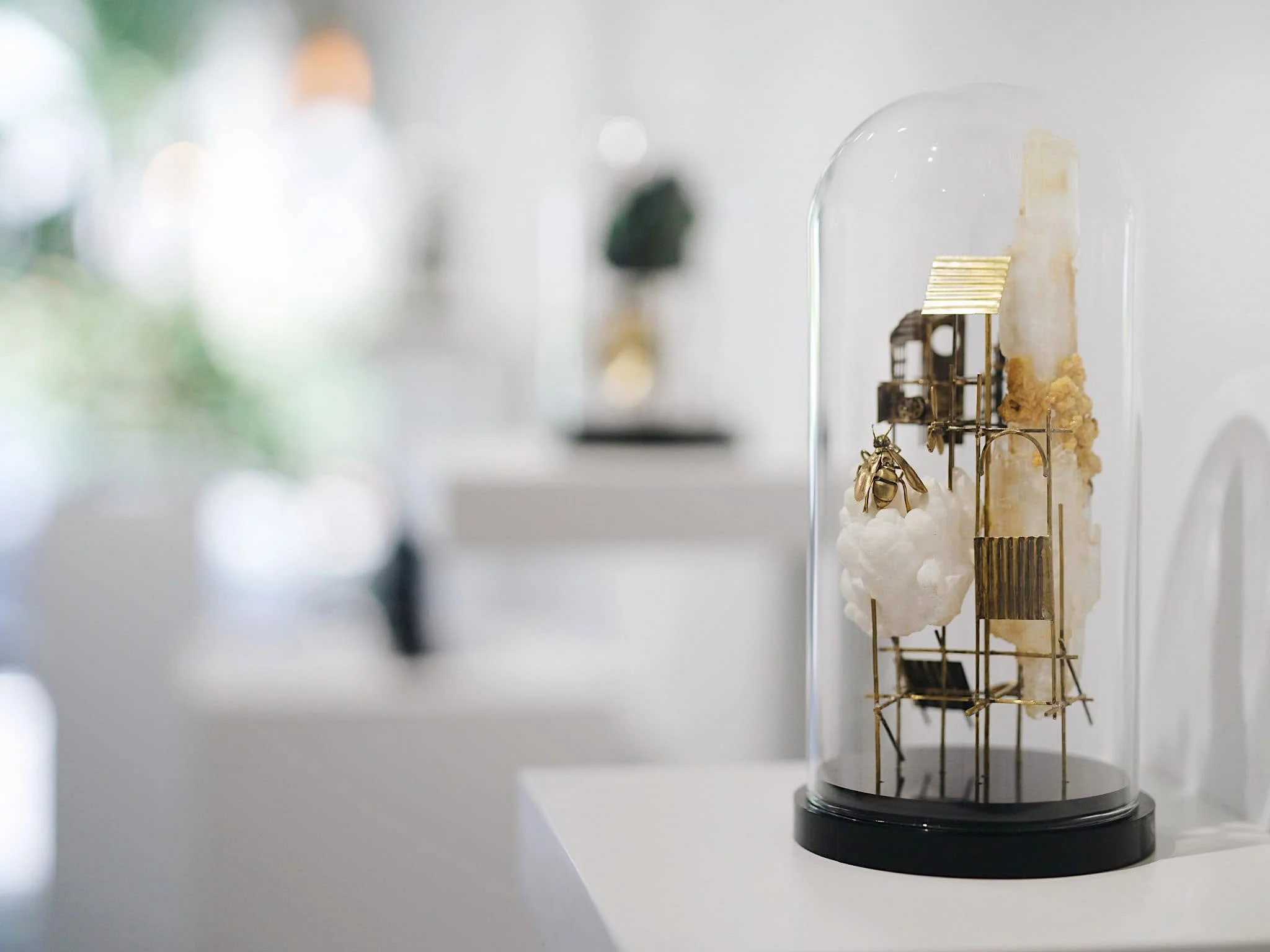 A glass display case with miniature architectural models inside, placed on a black base, with a blurred background of a gallery or exhibit space.