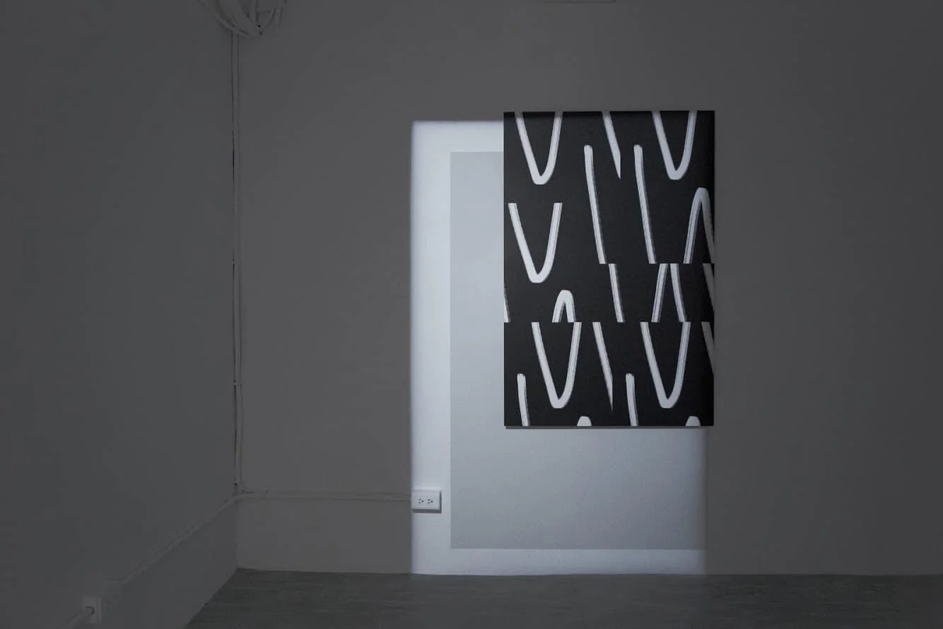 A gray wall with a black and white abstract canvas artwork and a rectangular window casting light onto the wall.