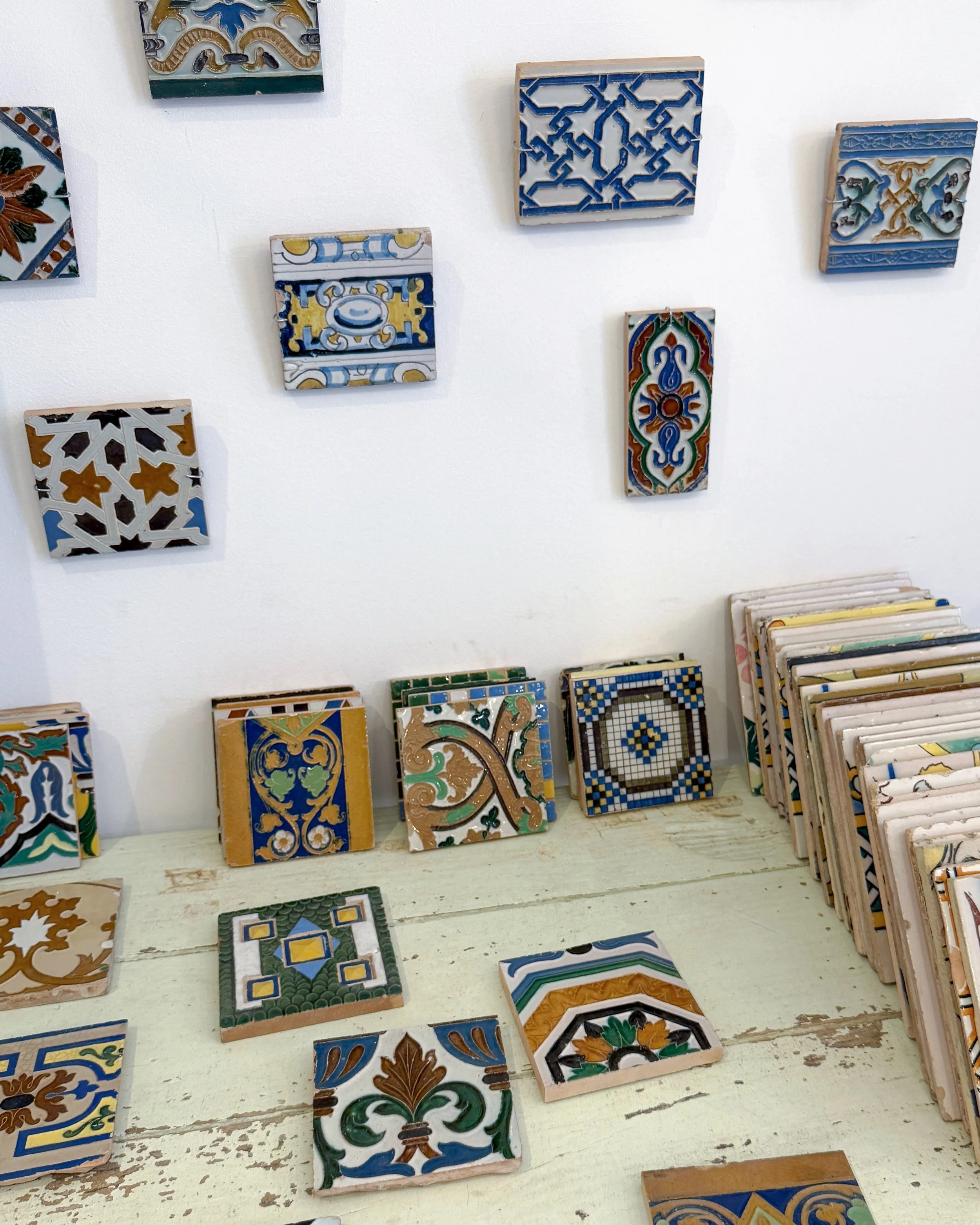 A collection of decorative ceramic tiles with colorful intricate patterns displayed on a white wall and a wooden surface.