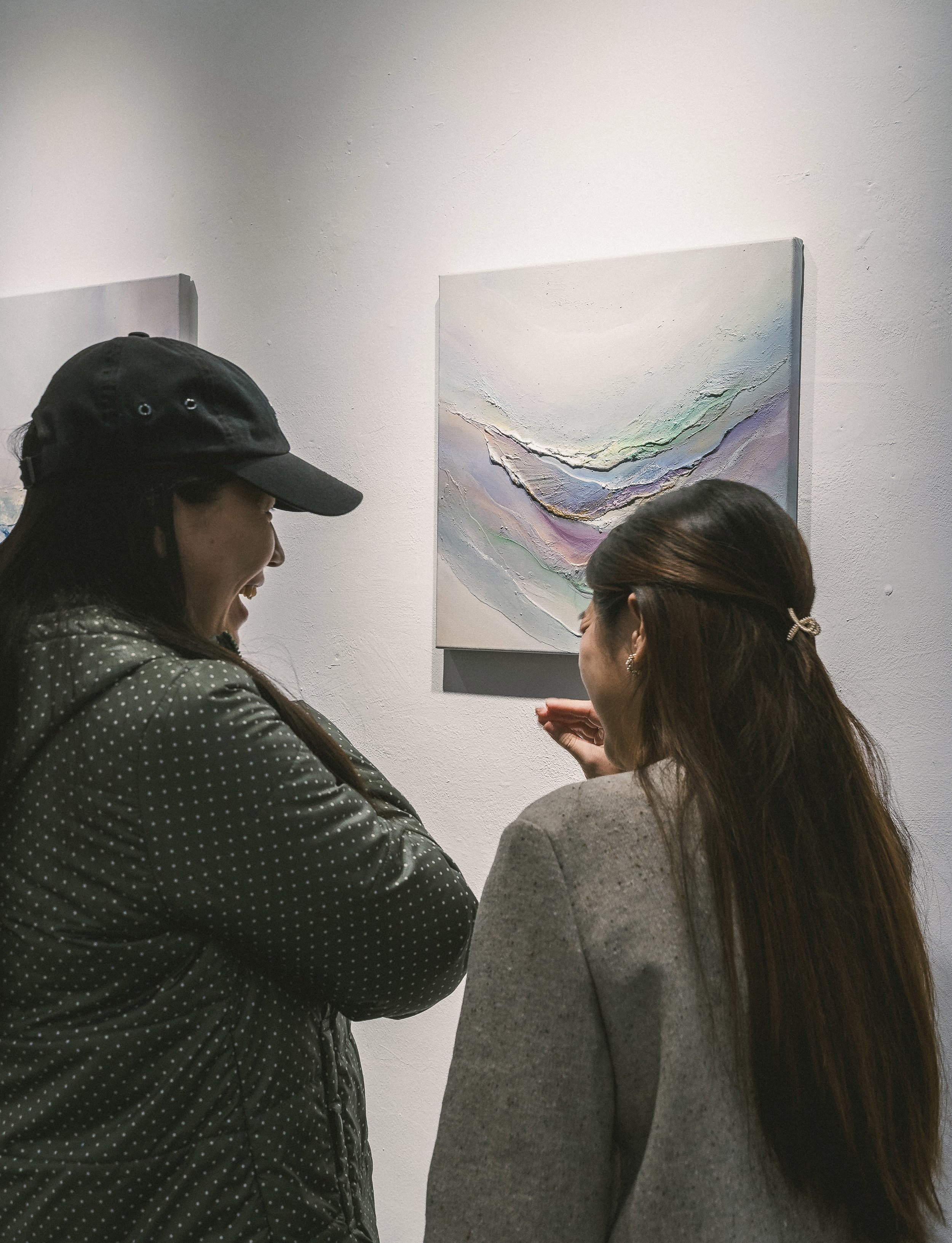 Two women talking in front of an abstract painting in an art gallery.