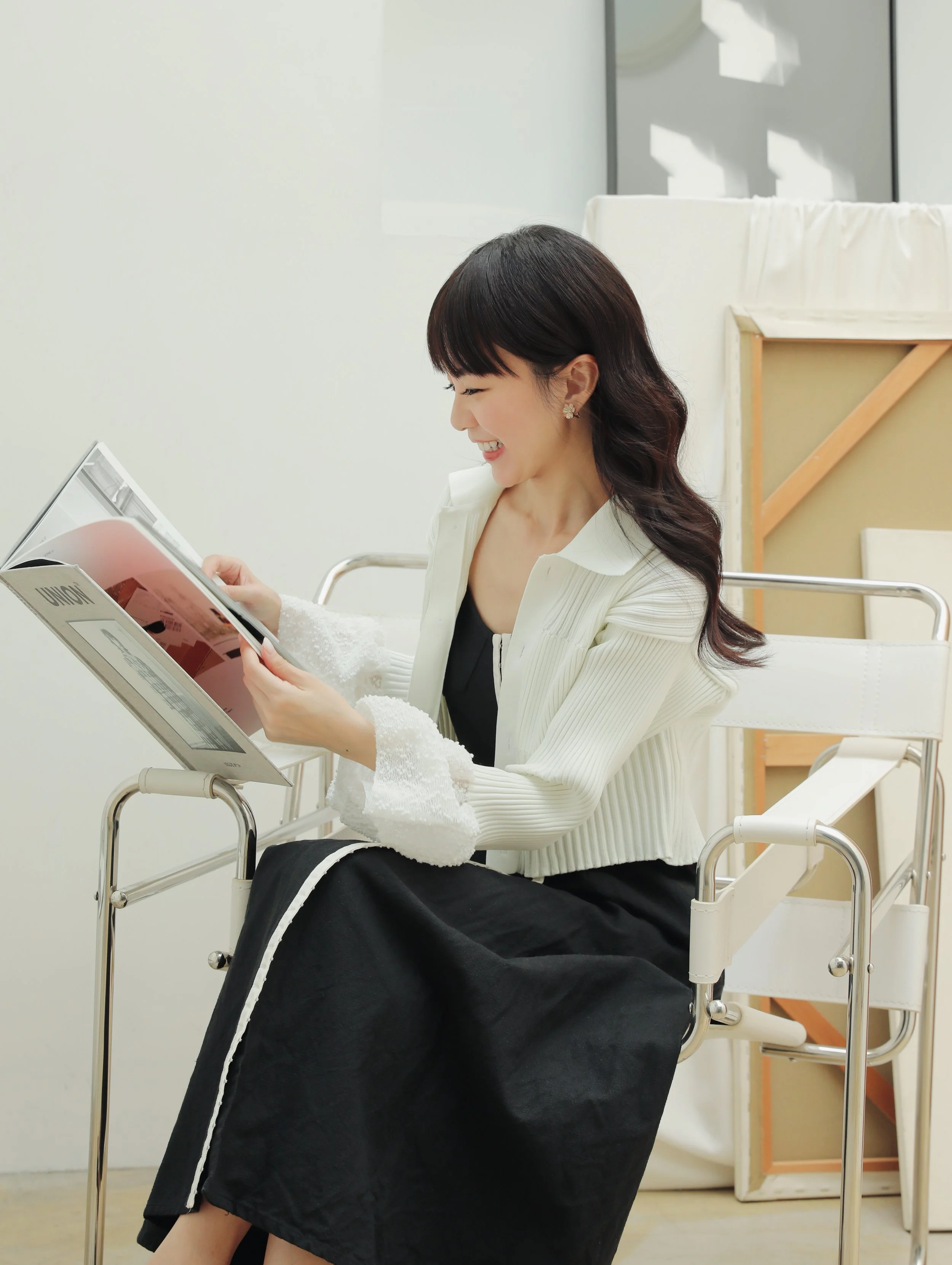 Smiling woman sitting in a wheelchair, reading a magazine in a bright, minimalistic room.