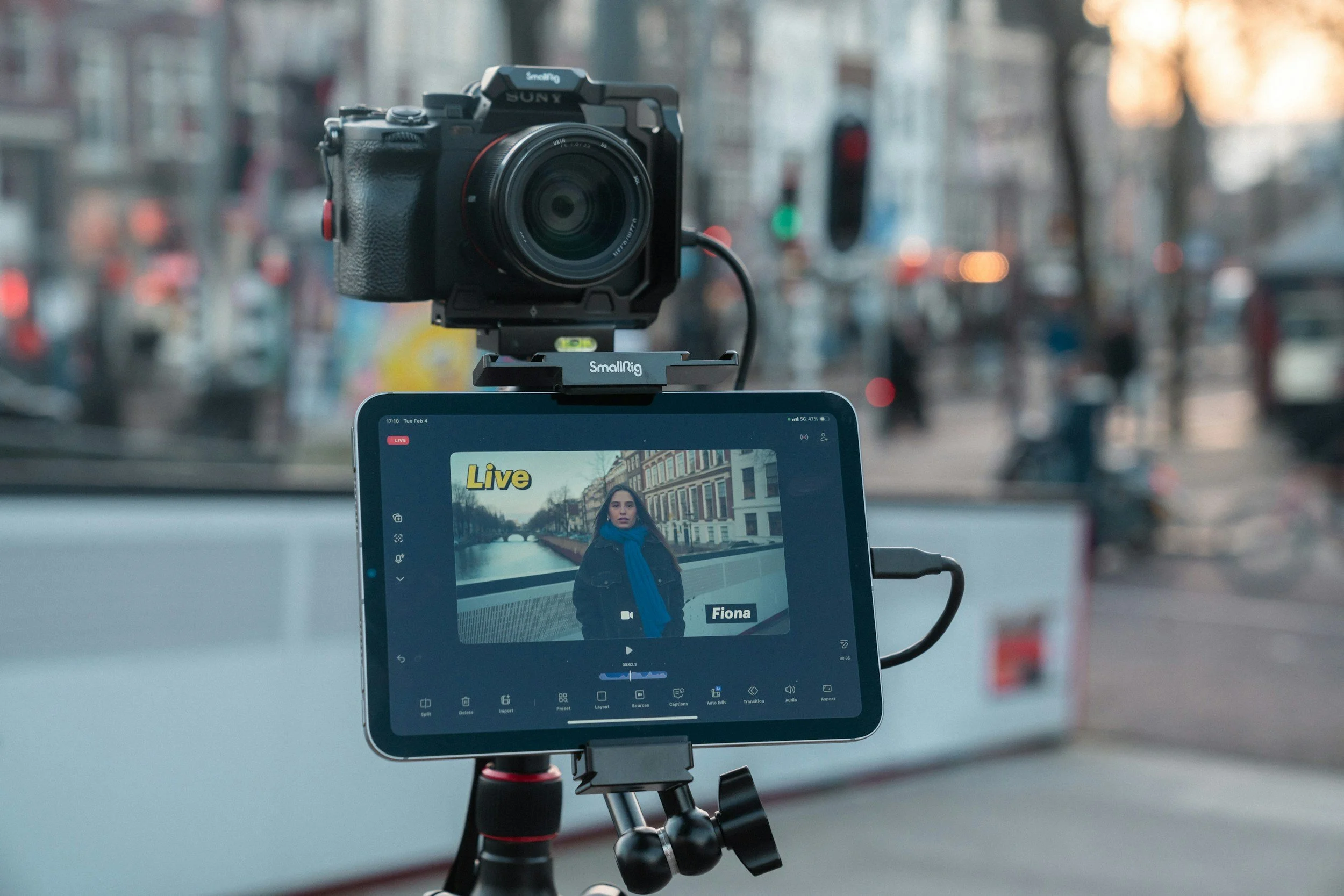A camera mounted on a smallRig rig setup, capturing footage of a woman with a blue scarf and dark coat standing on a canal bridge in a city town.