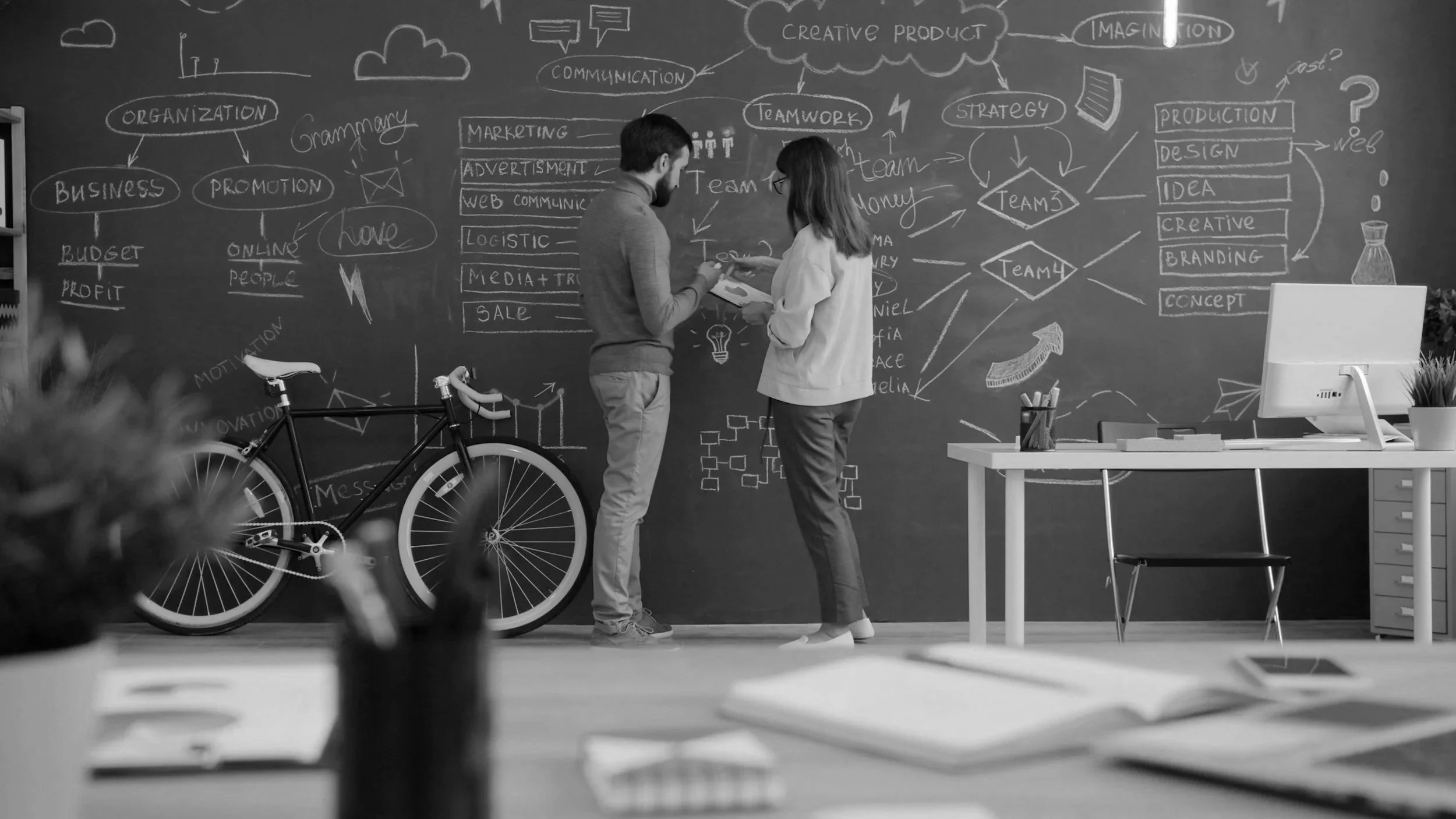Two marketers planning a growth strategy in front of a blackboard of ideas