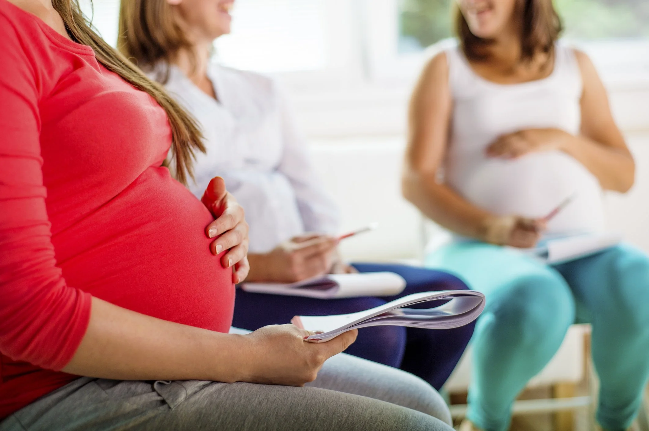 Several pregnant women sit in a group with notepads and pens, taking part in an antenatal class together.