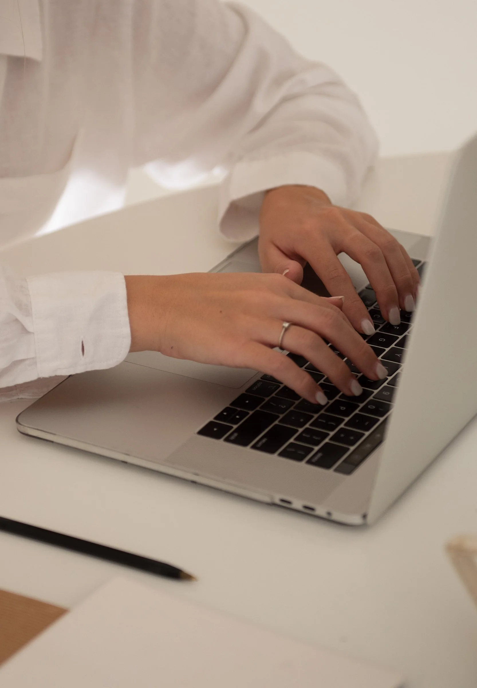 Person typing on a laptop keyboard, wearing a white shirt.