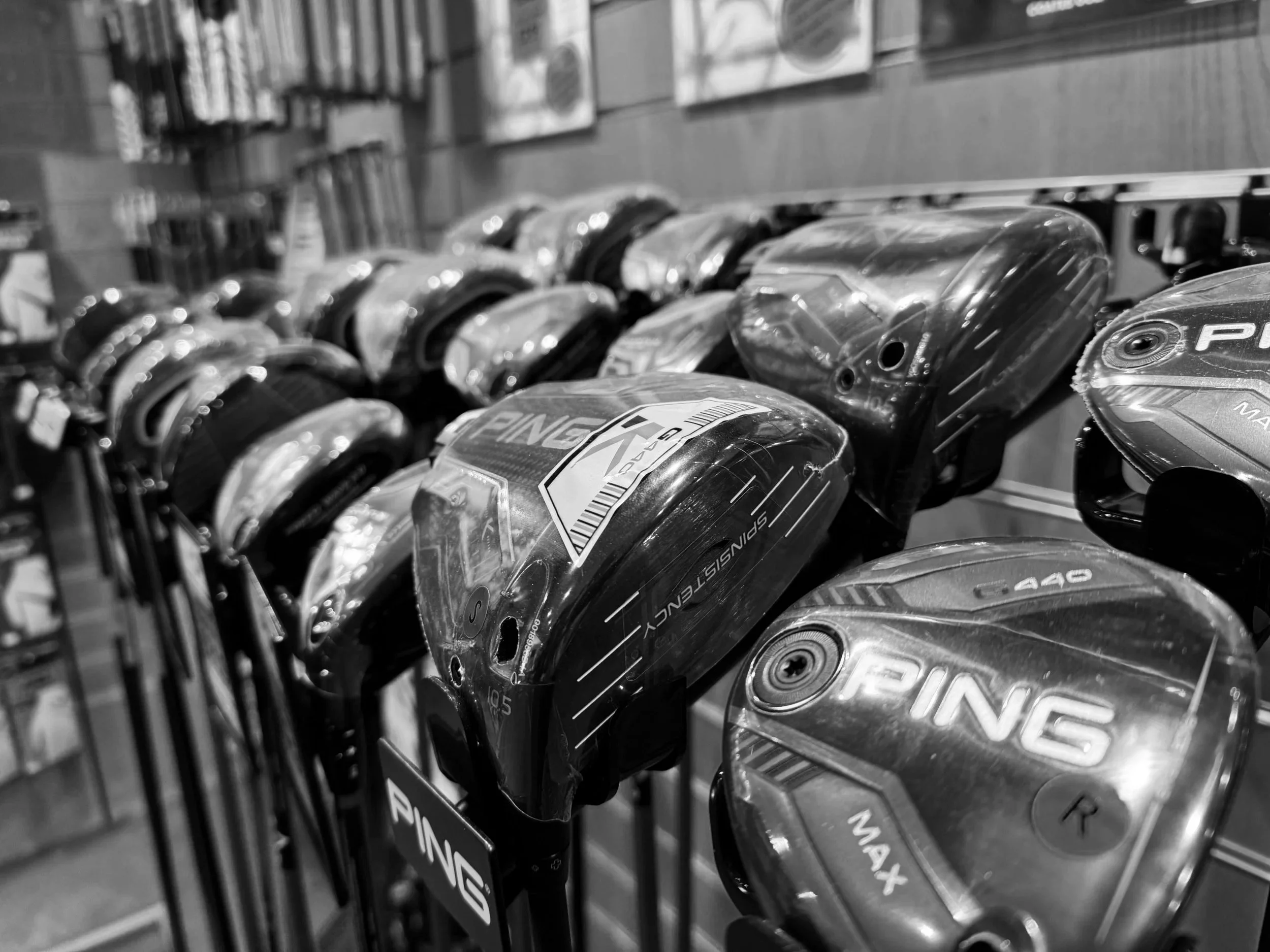 Close-up of a variety of golf clubs with labels such as driver, fairway wood, and hybrid displayed on their heads, arranged on a store shelf.