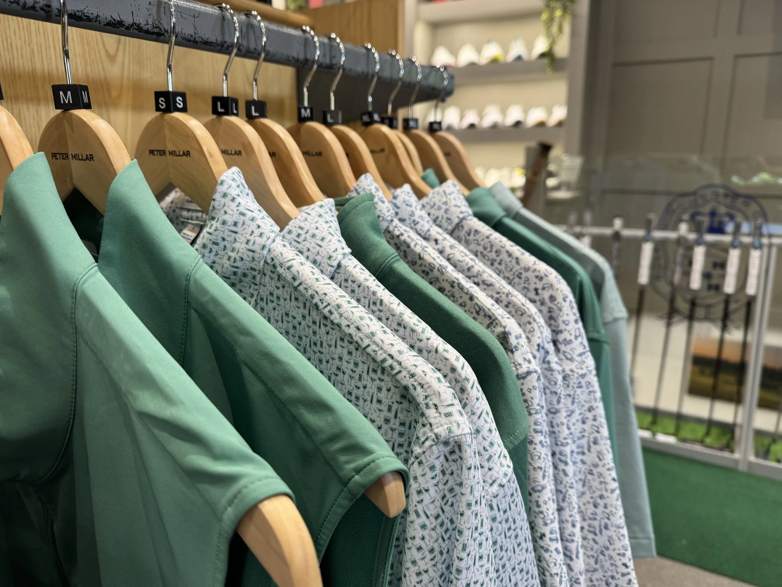 Clothing items on hangers, including green shirts and patterned shirts with white and blue designs, displayed on a rack in a store.